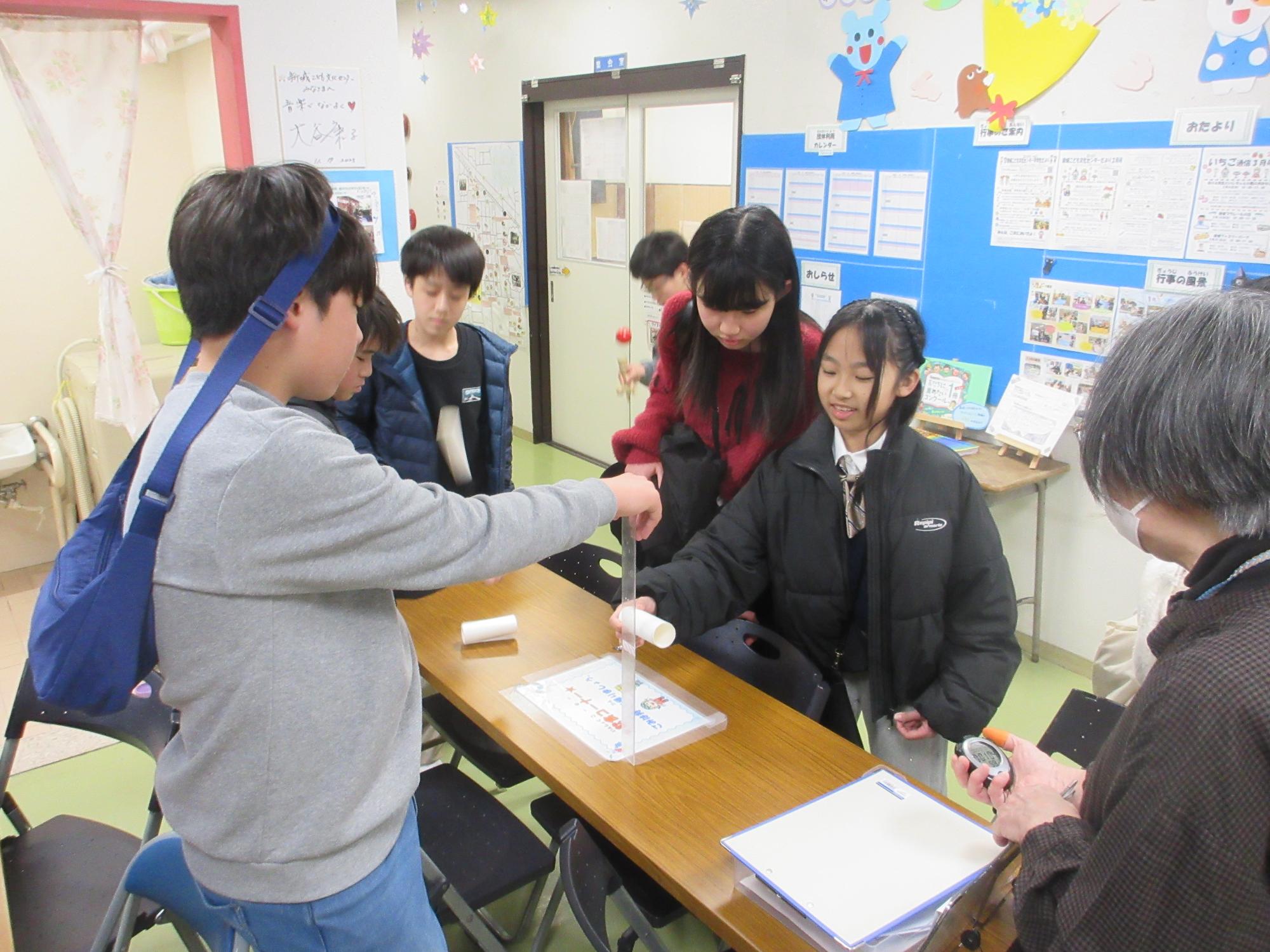 トイレットペーパーの芯を定規にあて20センチメートルの高さを確認する子ども