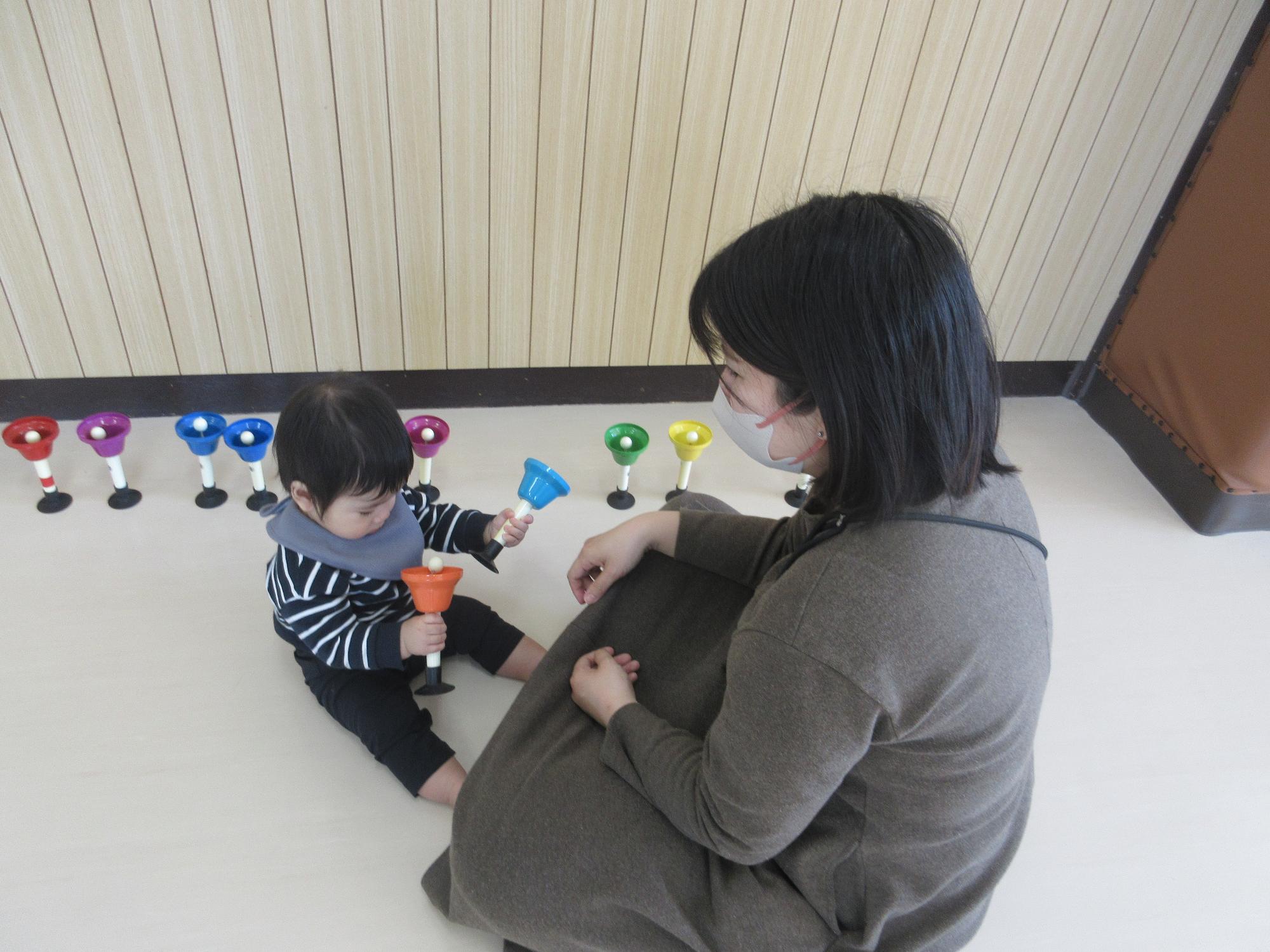 ハンドベルを両手に持って振る子どもと見守る母親