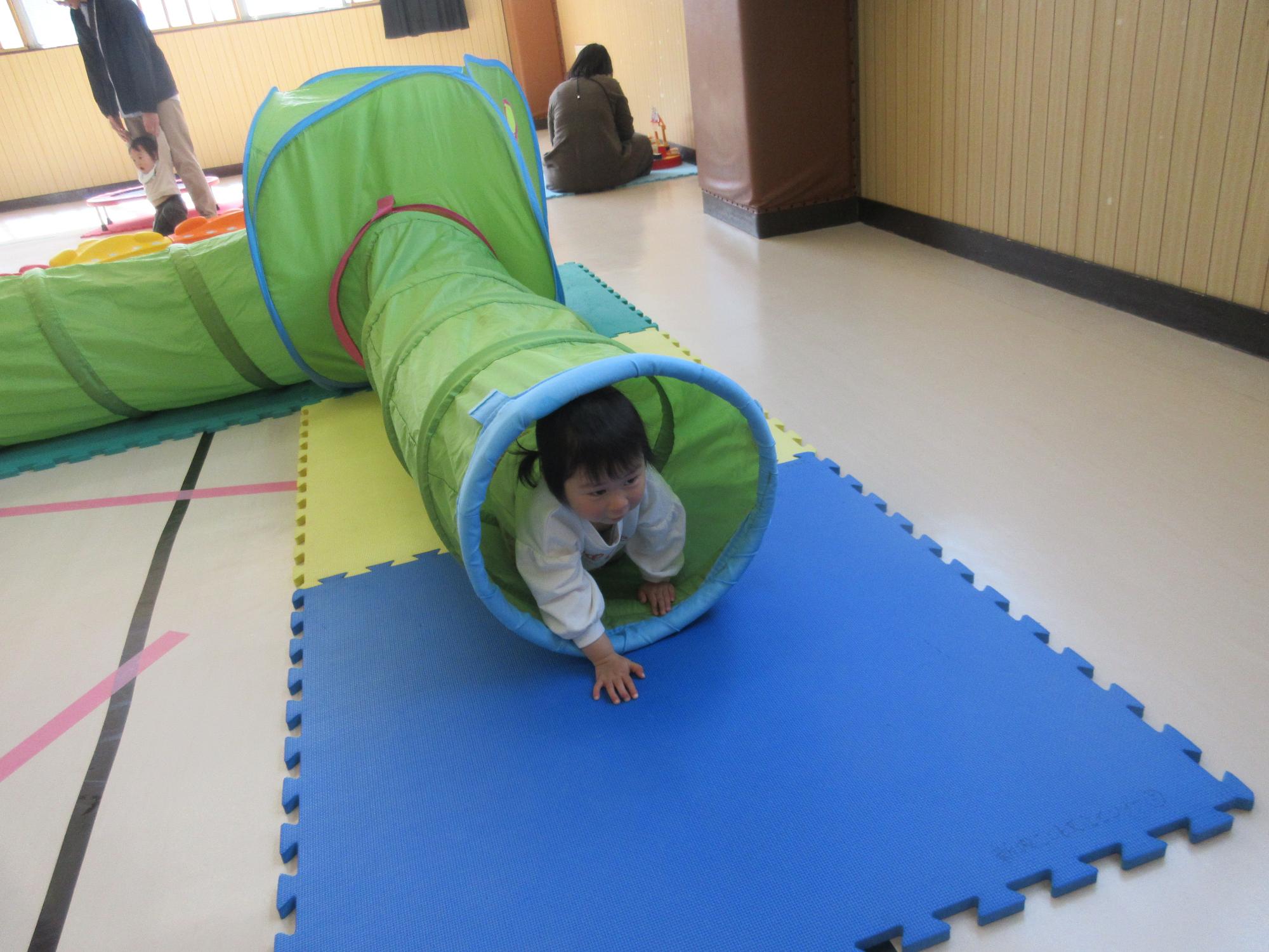 緑色の長いトンネルをハイハイで出てくるこども