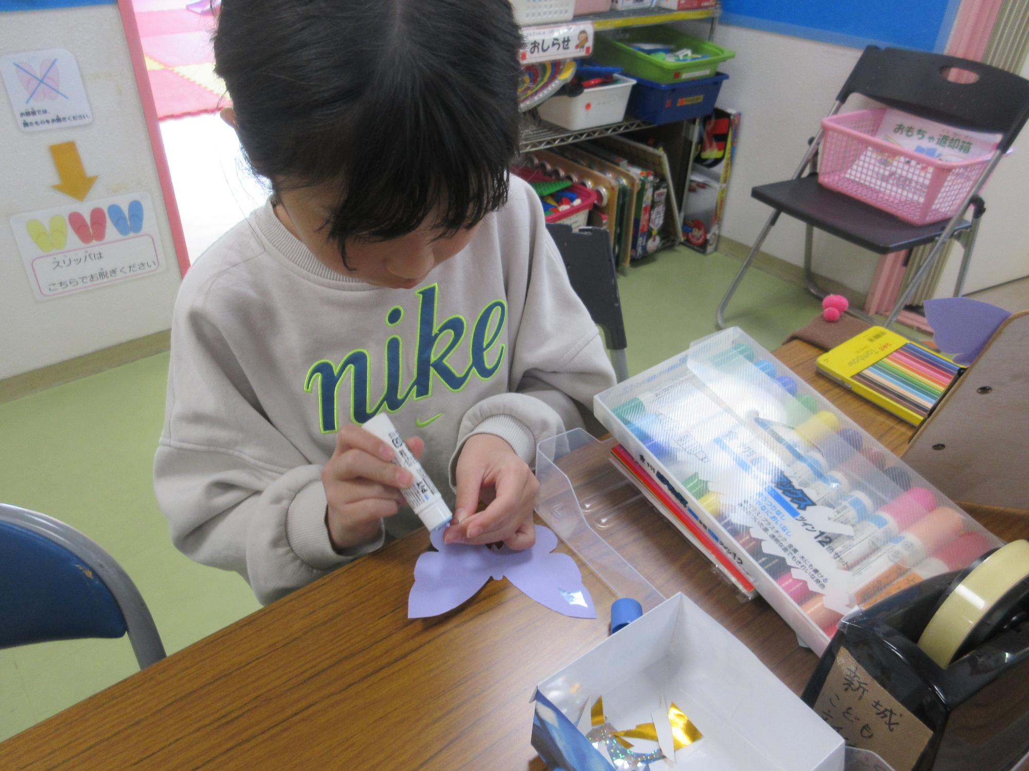 紫色のちょうに小さな金紙を乗りで貼り付ける子ども