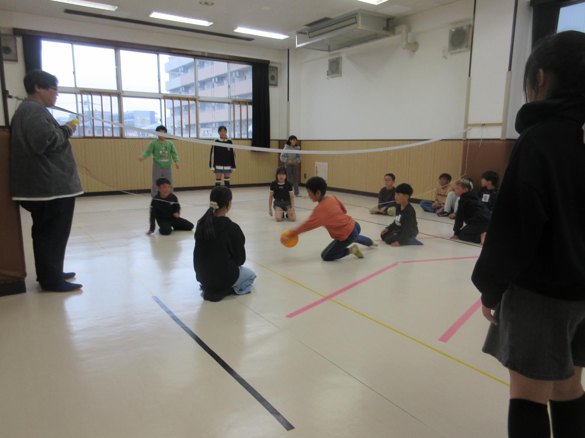 ネットの下から転がってきたボールを打ち返す子ども