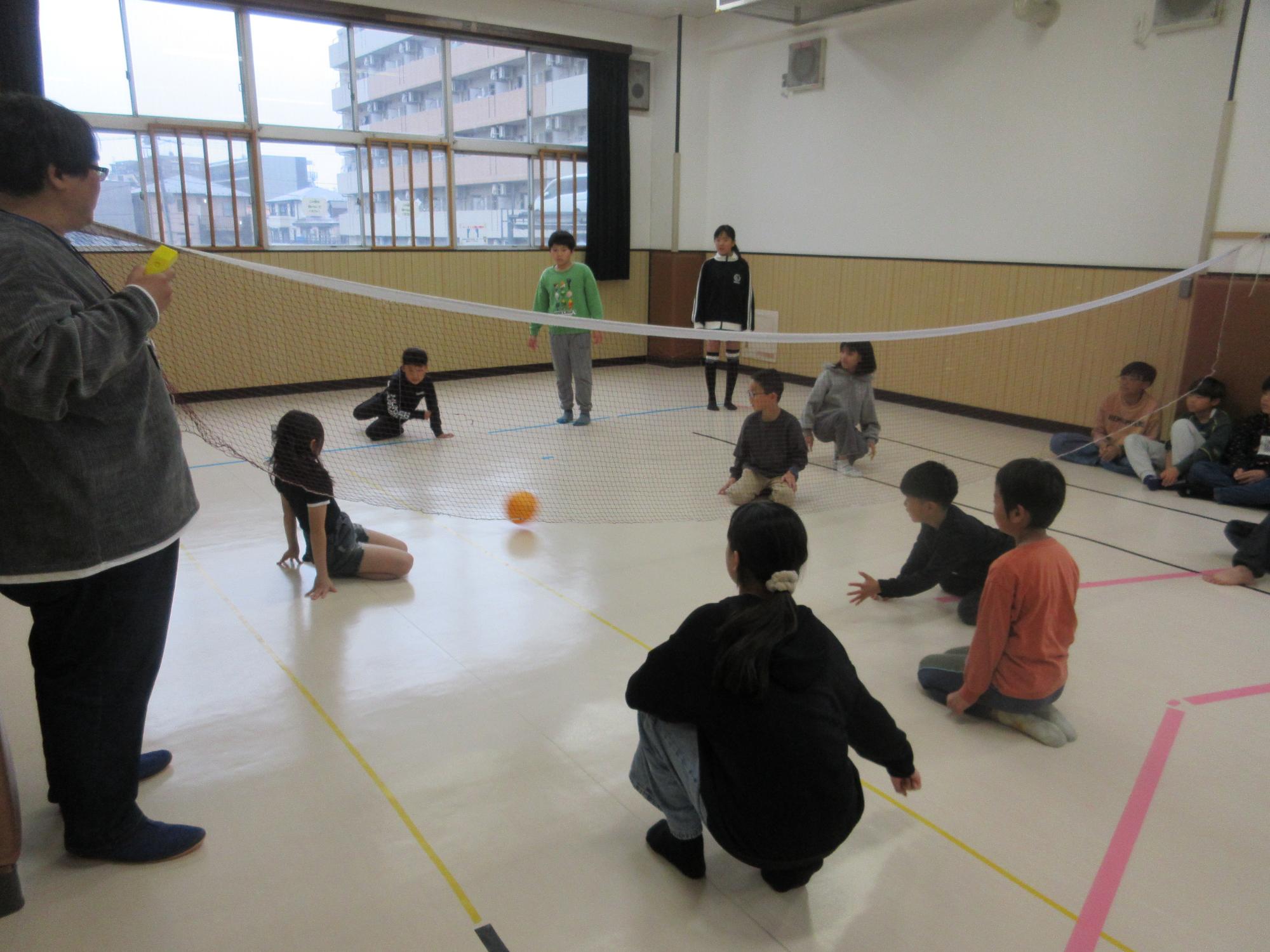 ネットをはさみ6人対6人に分かれボールを転がす子どもたち