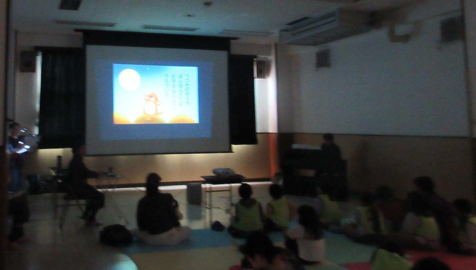 明かりを消した集会室でスクリーンに映る映像と音楽と物語をマットに座り見入る観客たち