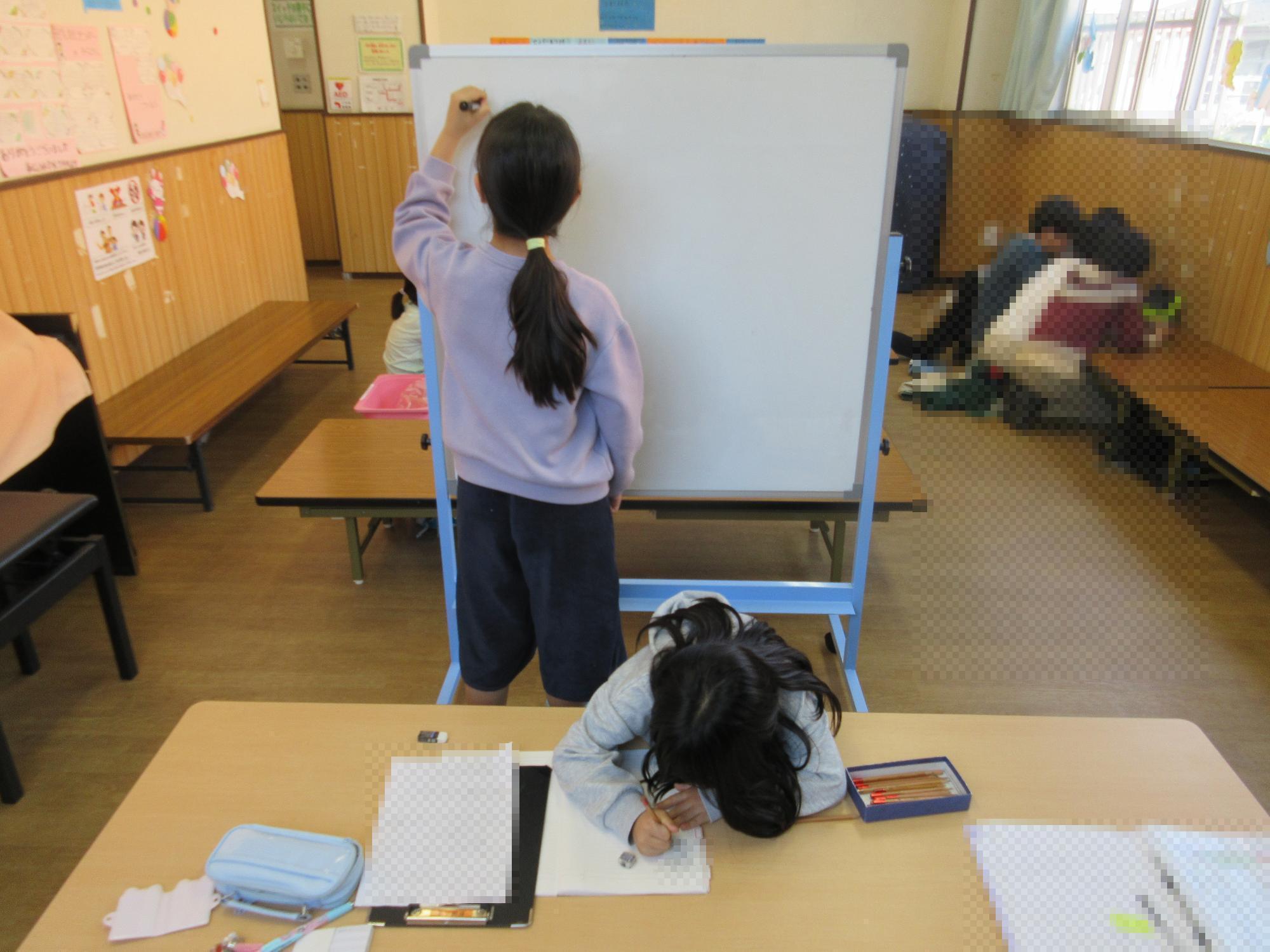 ホワイトボードに集めた意見を書き出すこどもとテーブルで議事録ノートに記入するこども