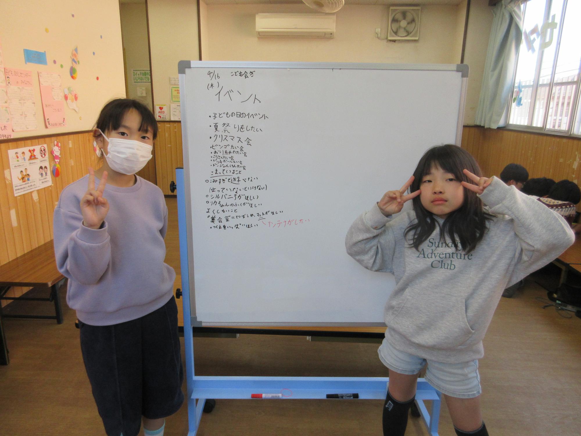 会議の記録を書いたホワイトボードの前に立つ2人のこども