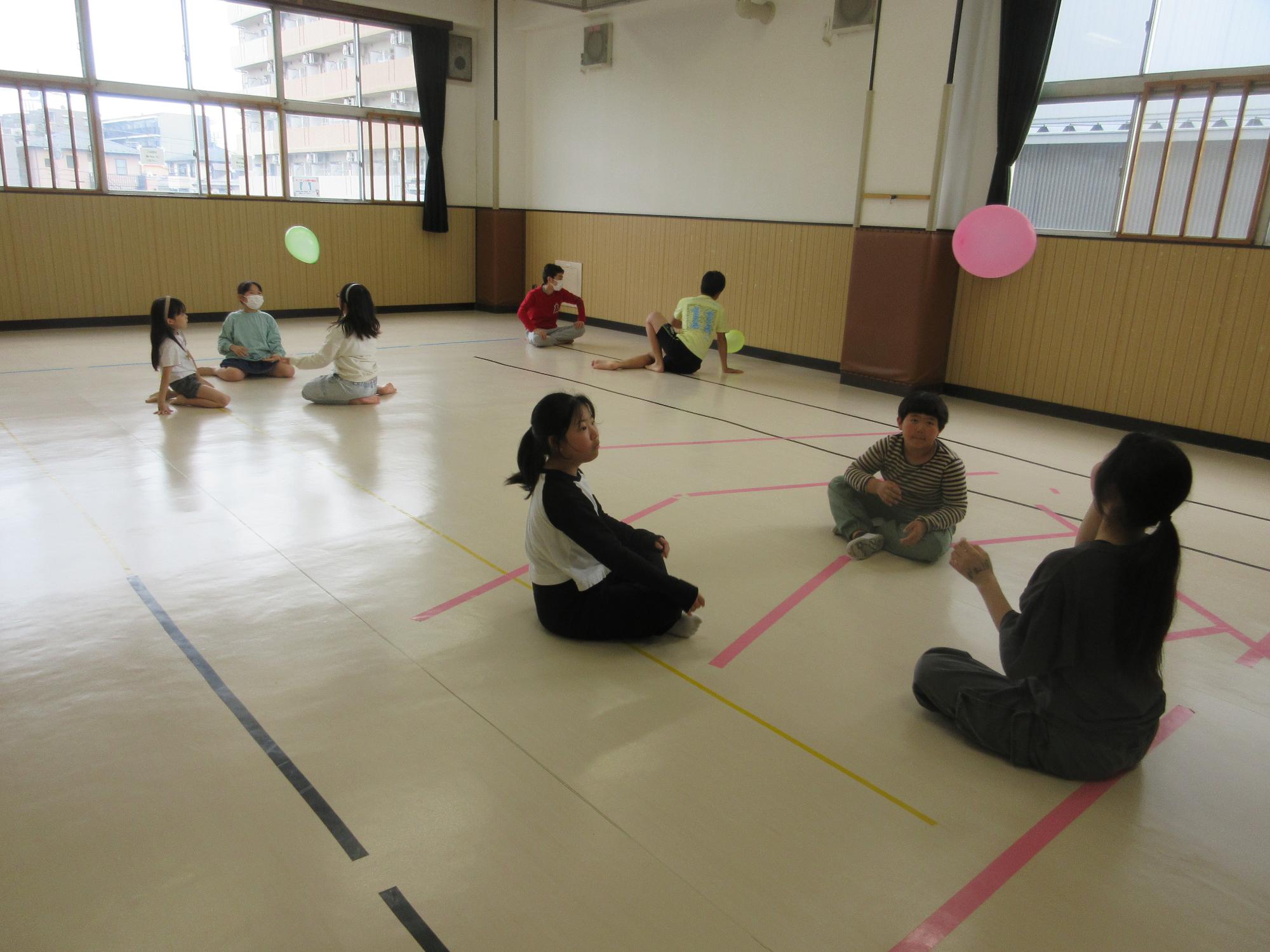小中学生が3人グループが2組、2人グループが1組が床に座り風船をパスしているところ