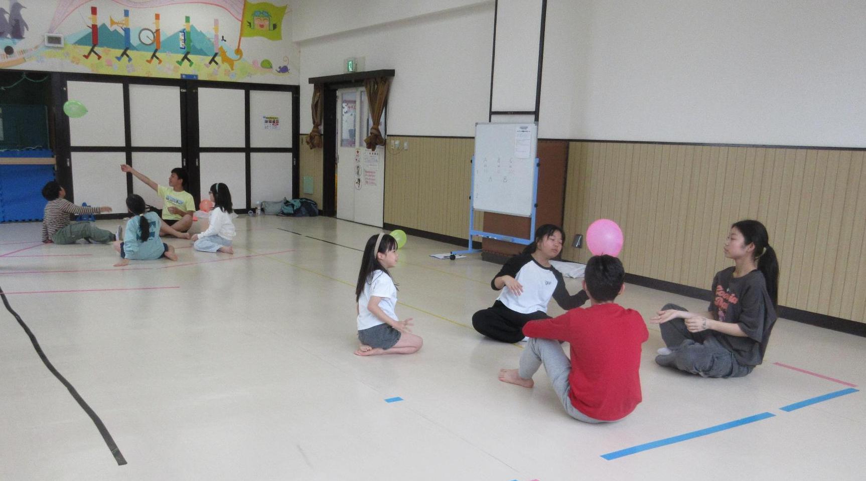 小中学生が4人ずつ2組になり床に輪になり座り風船をとばしているところ