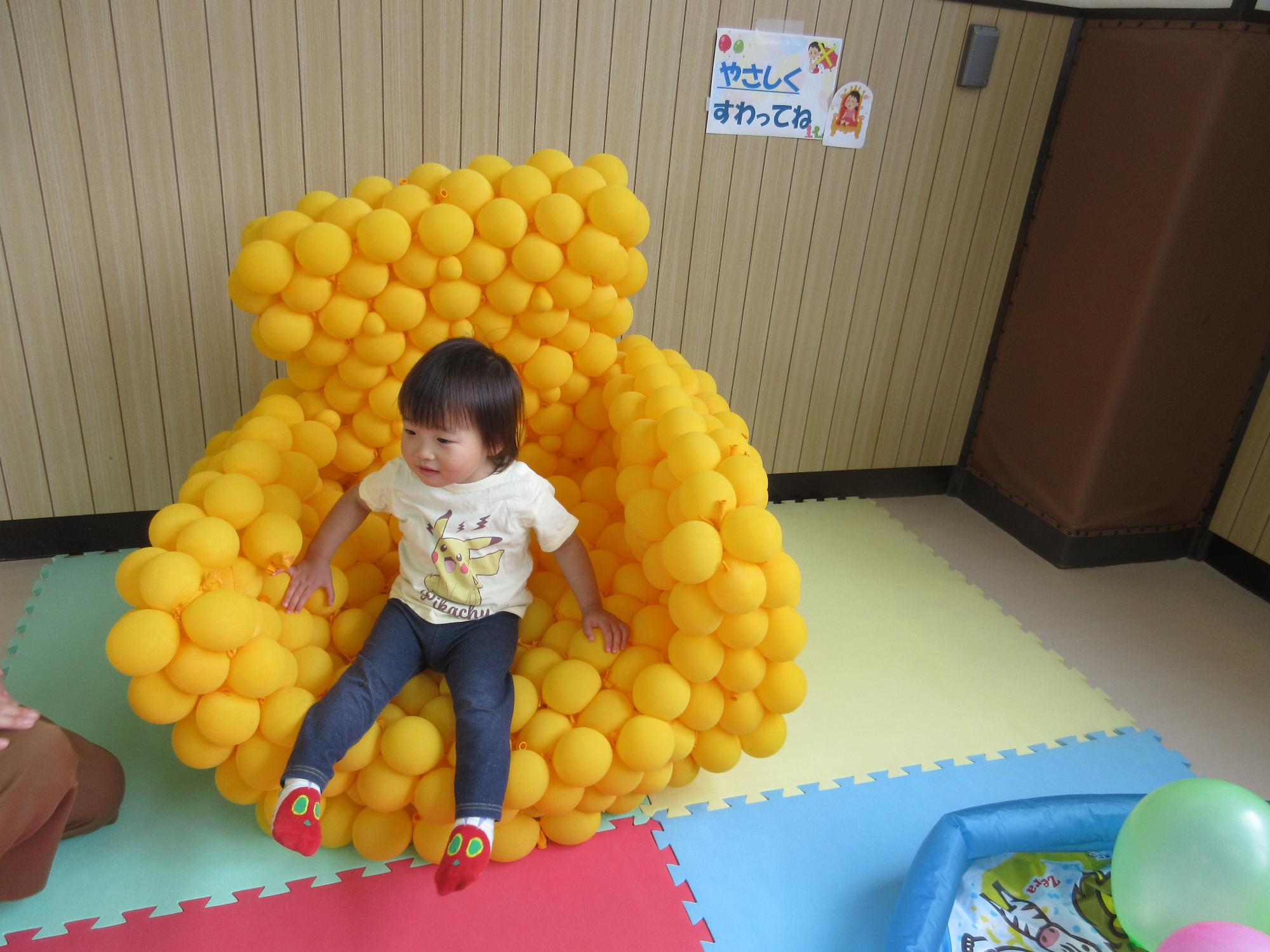 黄色の風船でできたソファに体を沈めて座るこども