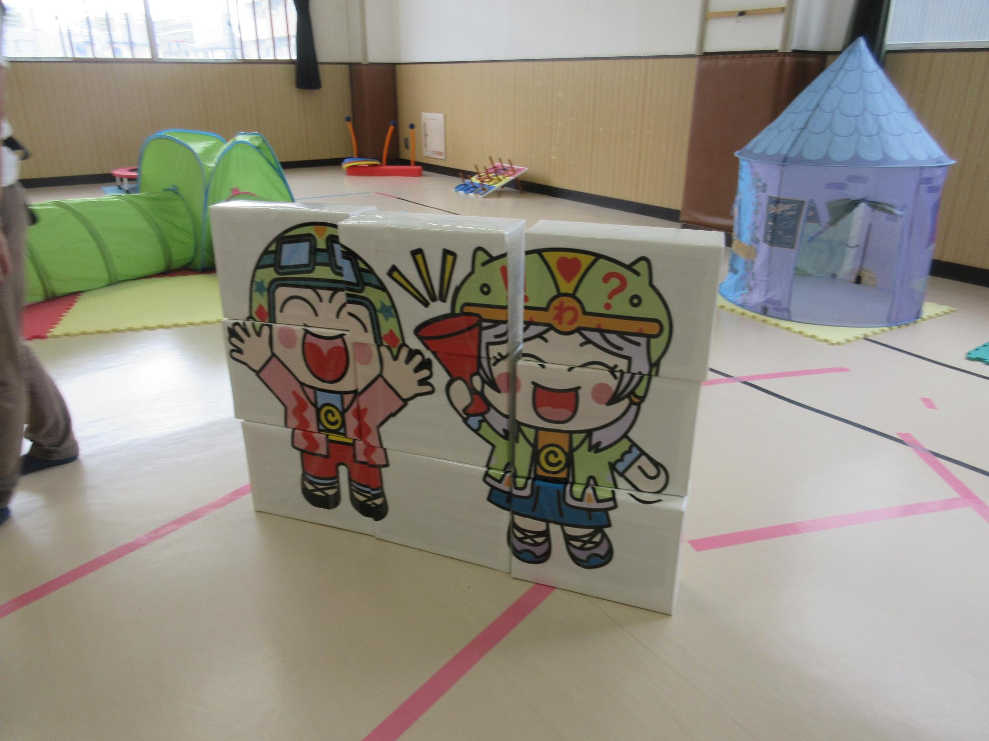 こどもの背丈くらいのこぶんたとわくりんの絵が描かれた縦3個横3個の合計9個の立体パズル