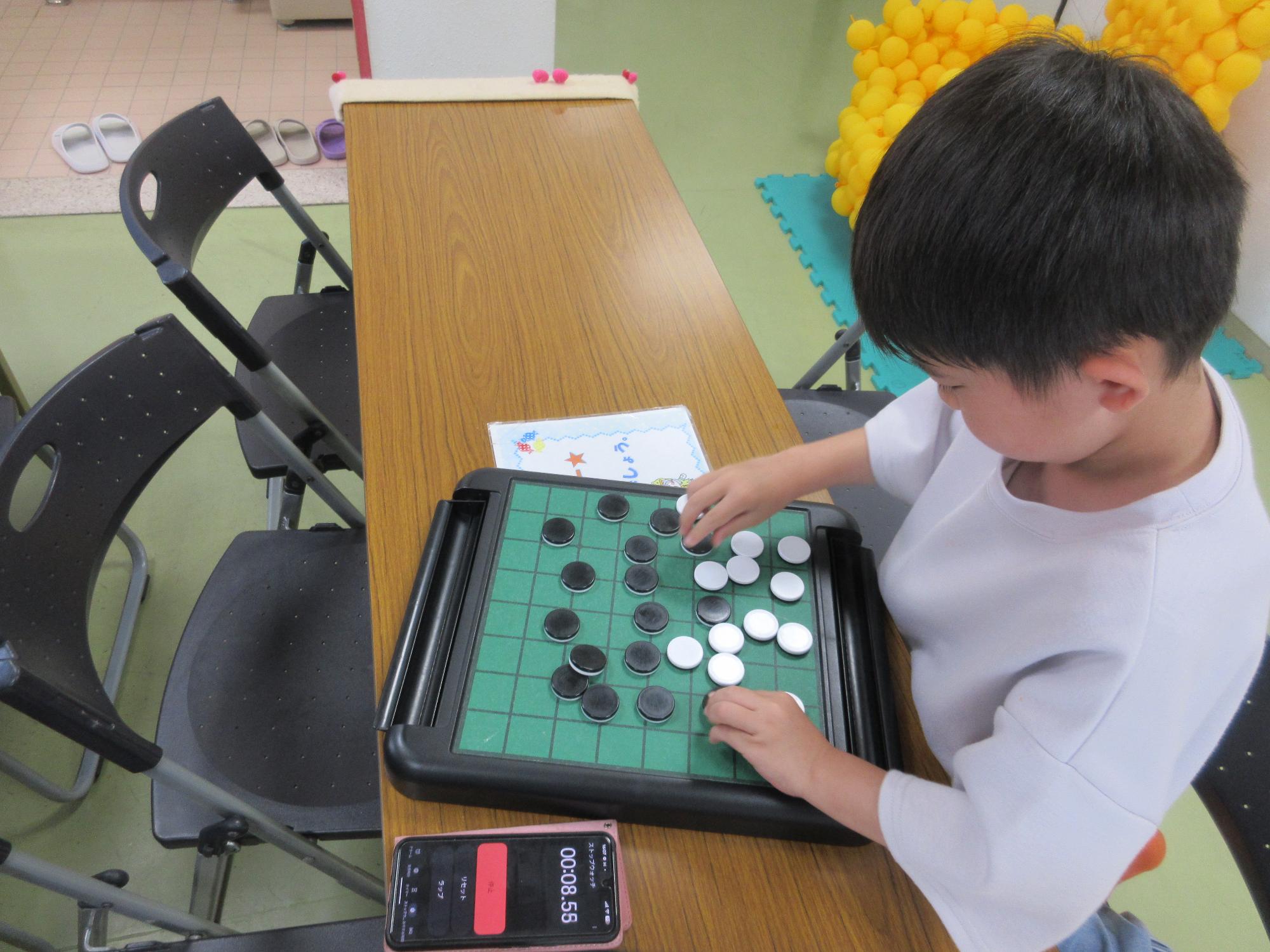 小学生がオセロ盤の上の30個の駒を両手でひっくり返し半分色をそろえたところ