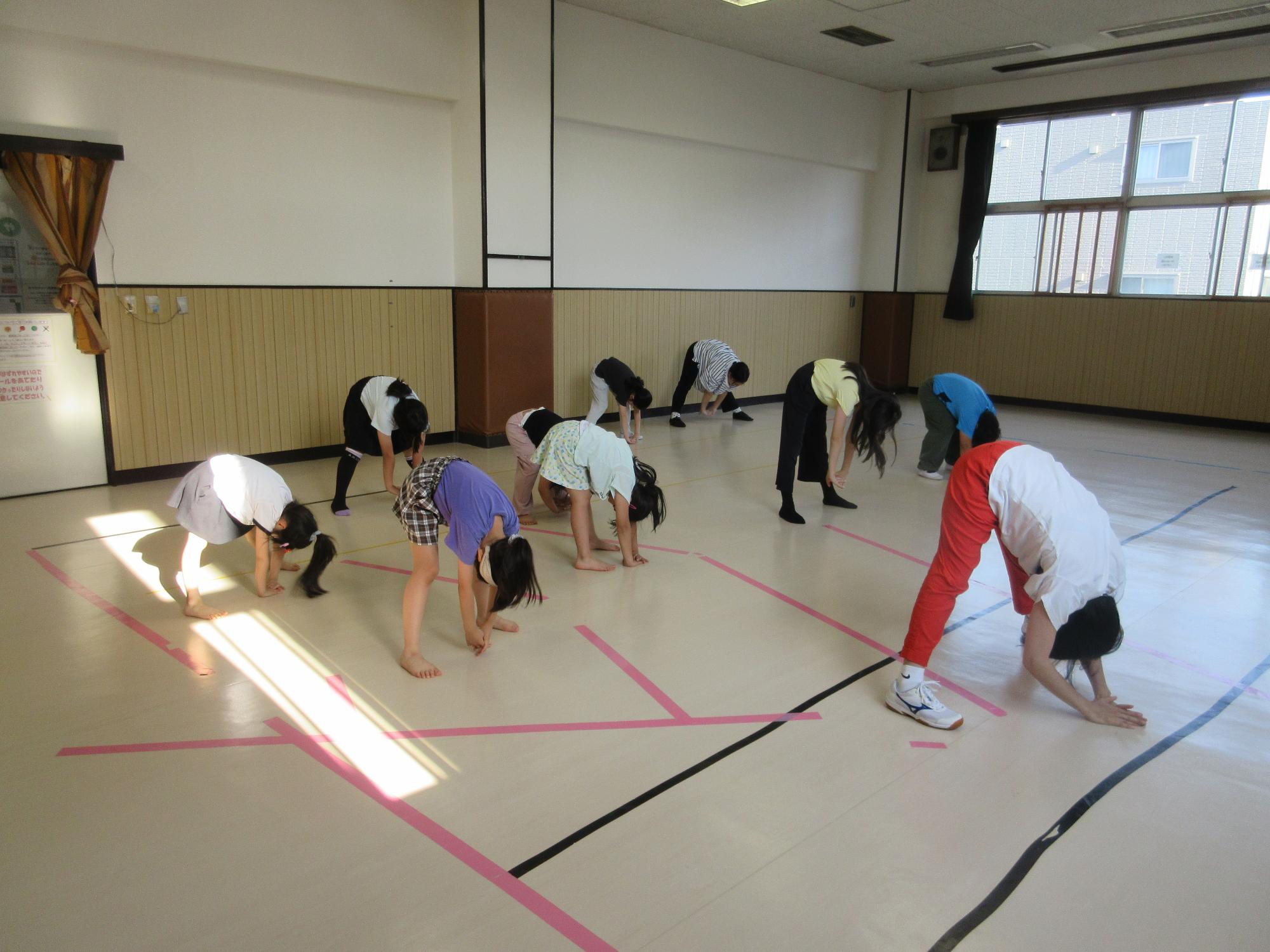 講師が前に立ち手本となり、子どもが二列に並び立って足を開き前屈をする様子