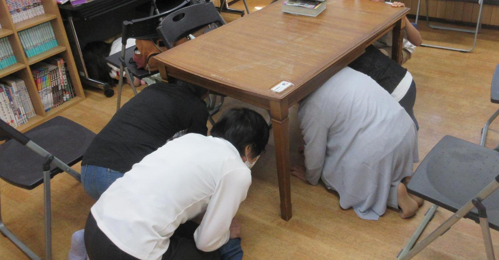 図書室でイスをよけテーブルの下に頭を隠して避難する様子