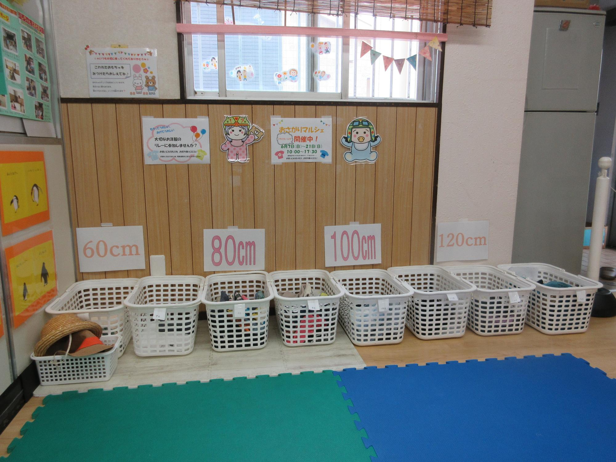 いちごルームで60cm80cm100cm120cmの表示の下に10cmごとにサイズ分けした服が白いかごにはいり並んでおいてあるところ