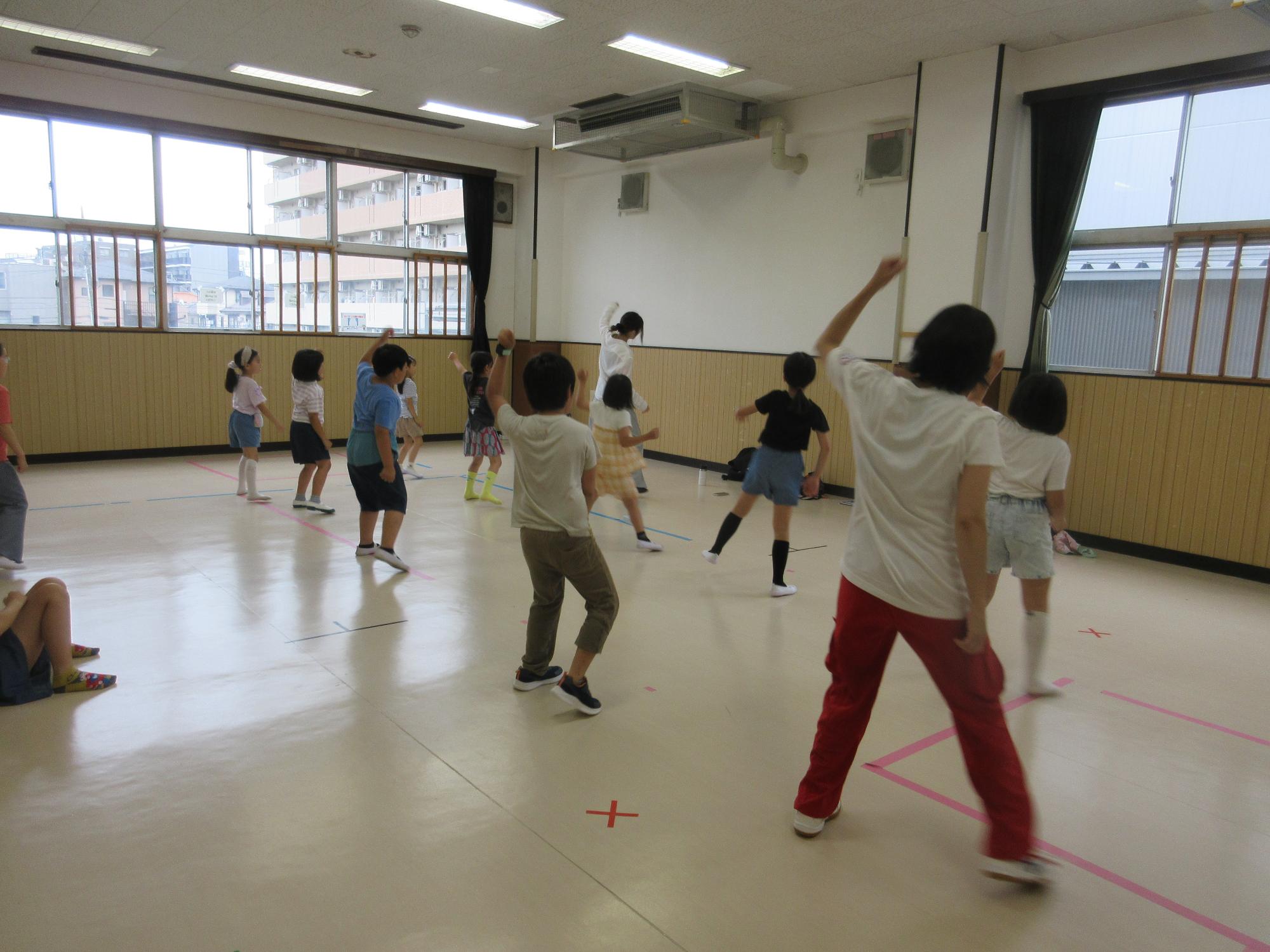 二列に並び先生の手本を見ながら左手をあげてサイドステップをする子どもたち