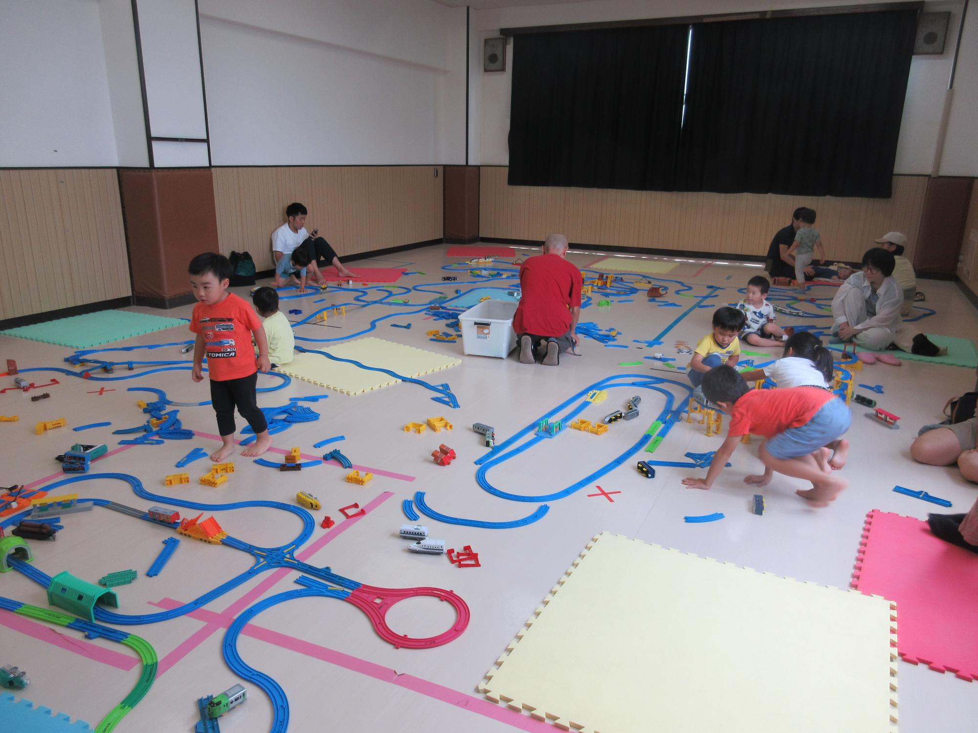 集会室で所狭しとレールをつなげ電車を走らせtる子どもたちと見守る親たち