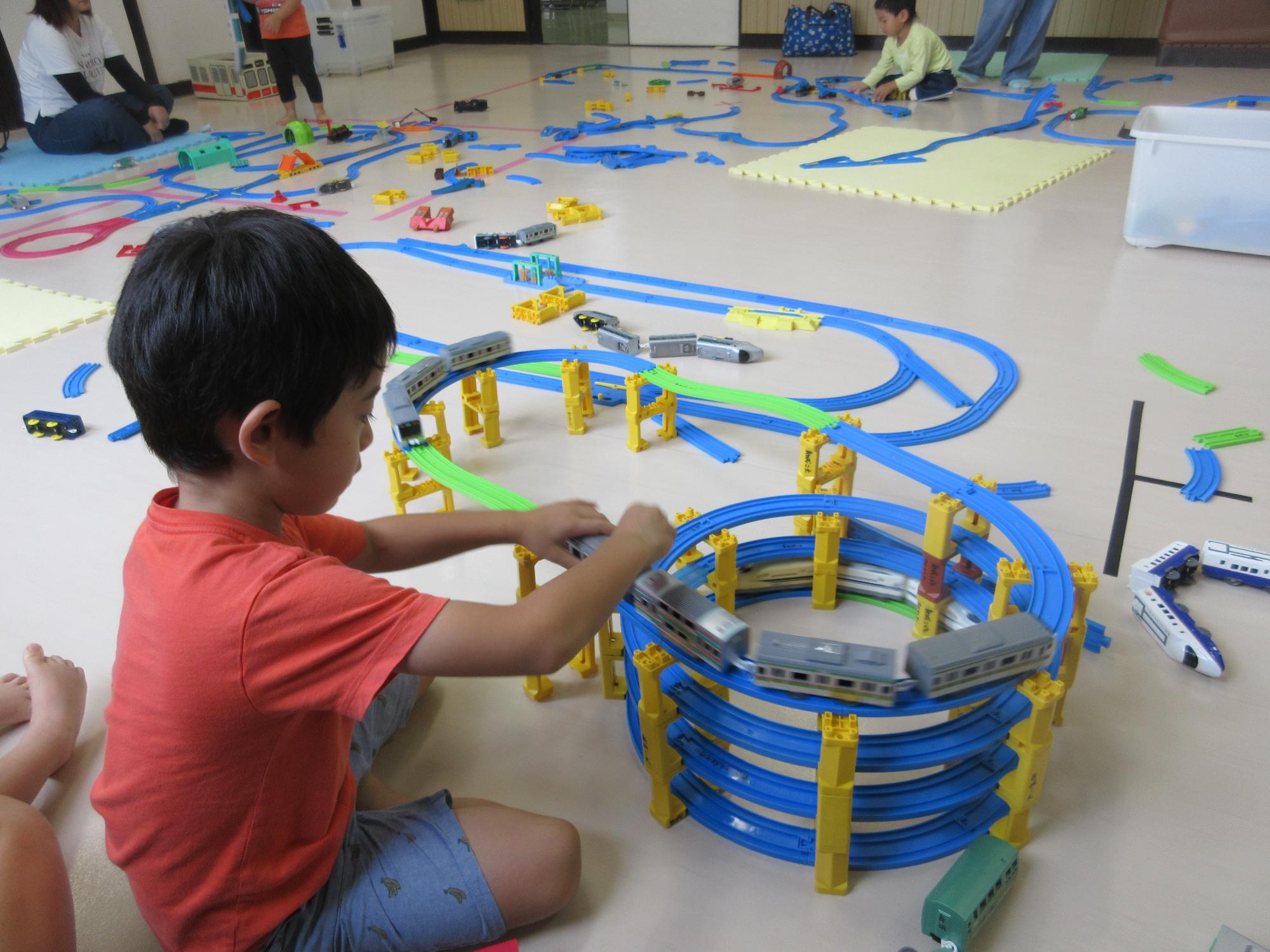 円い4段の線路を作り電車を走らせ上り下りをさせて遊ぶ座っている子ども