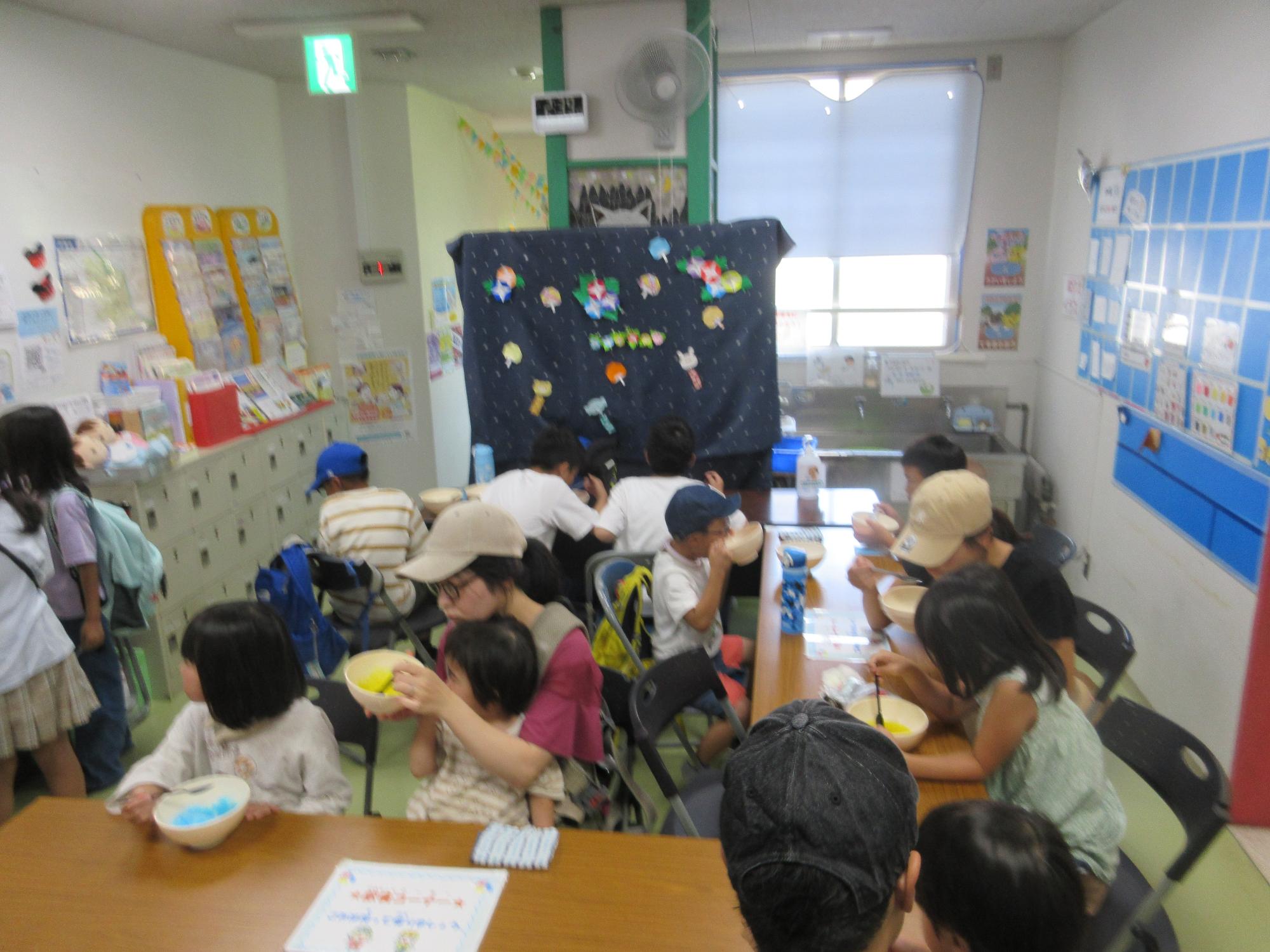 ホールでコの字型に配置っされたテーブルでかき氷を食べる来館者