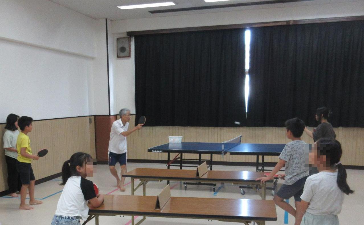 卓球台をはさみシニアの方とラリーをする中学生
