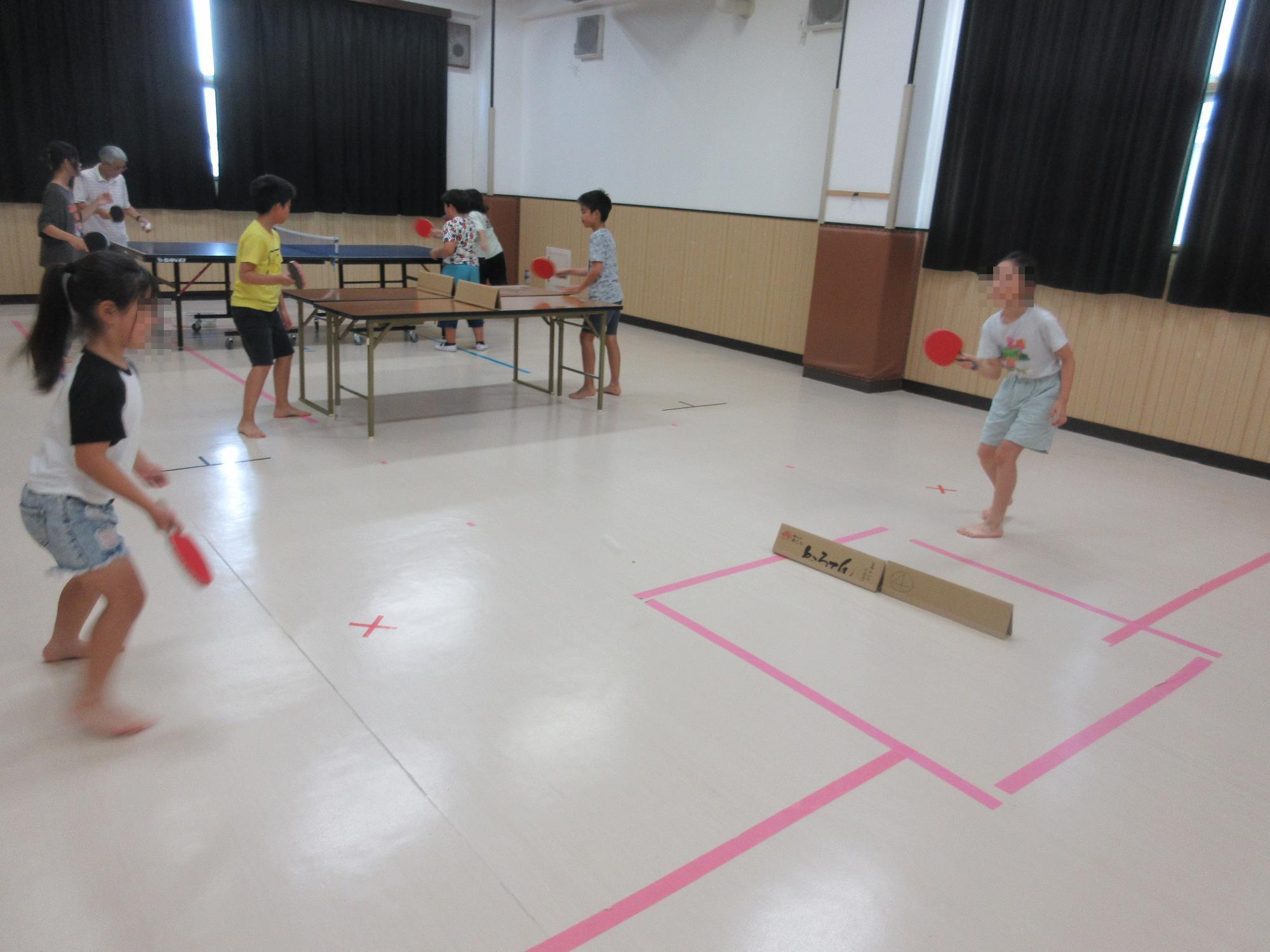 長テーブルを2台つなげた卓球台と床にネットの代わりにダンボールをおいたスペースでラリーをする子どもたち