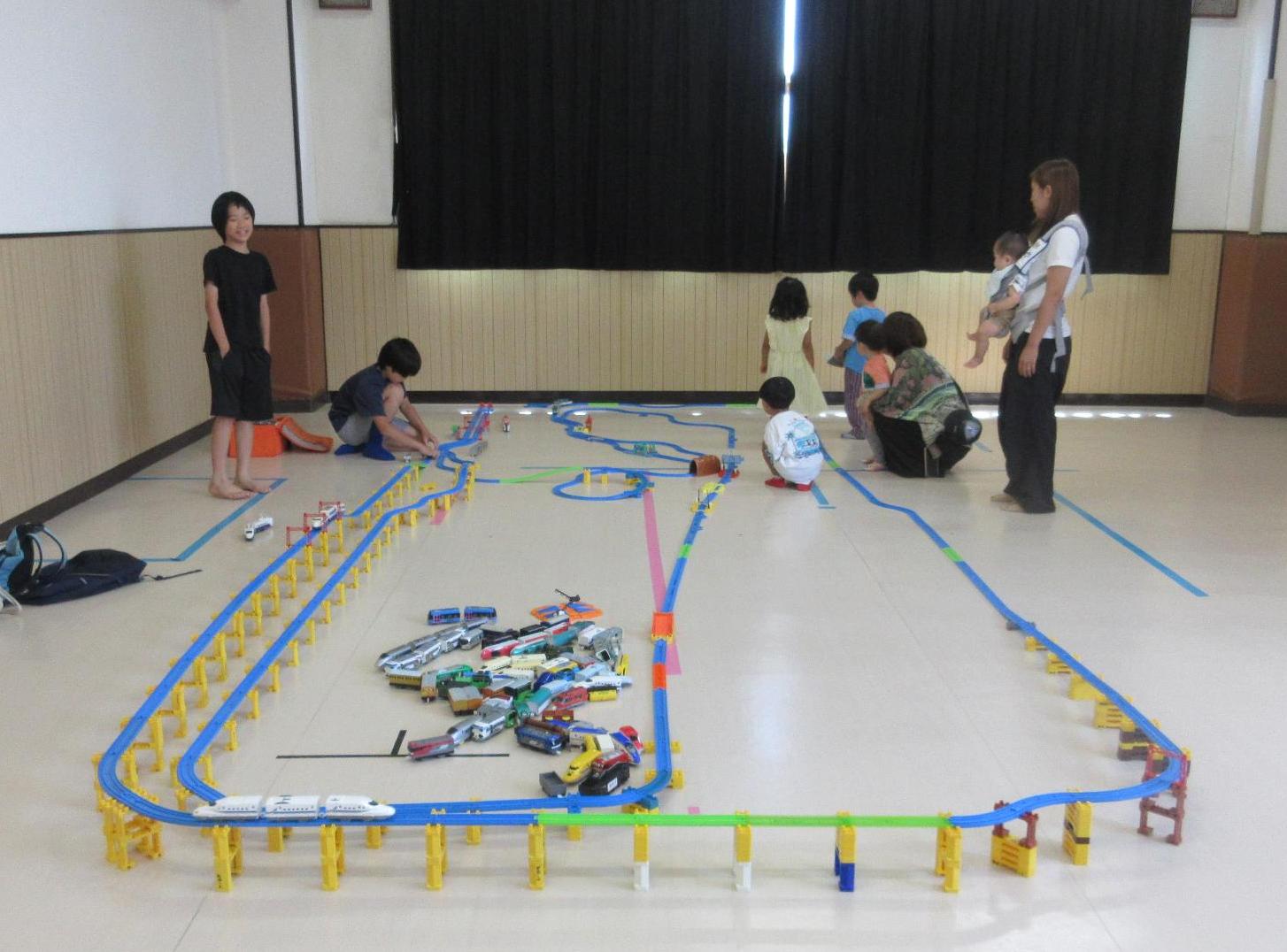 小学生の作った大きな線路のプラレールを見て楽しむ幼児親子
