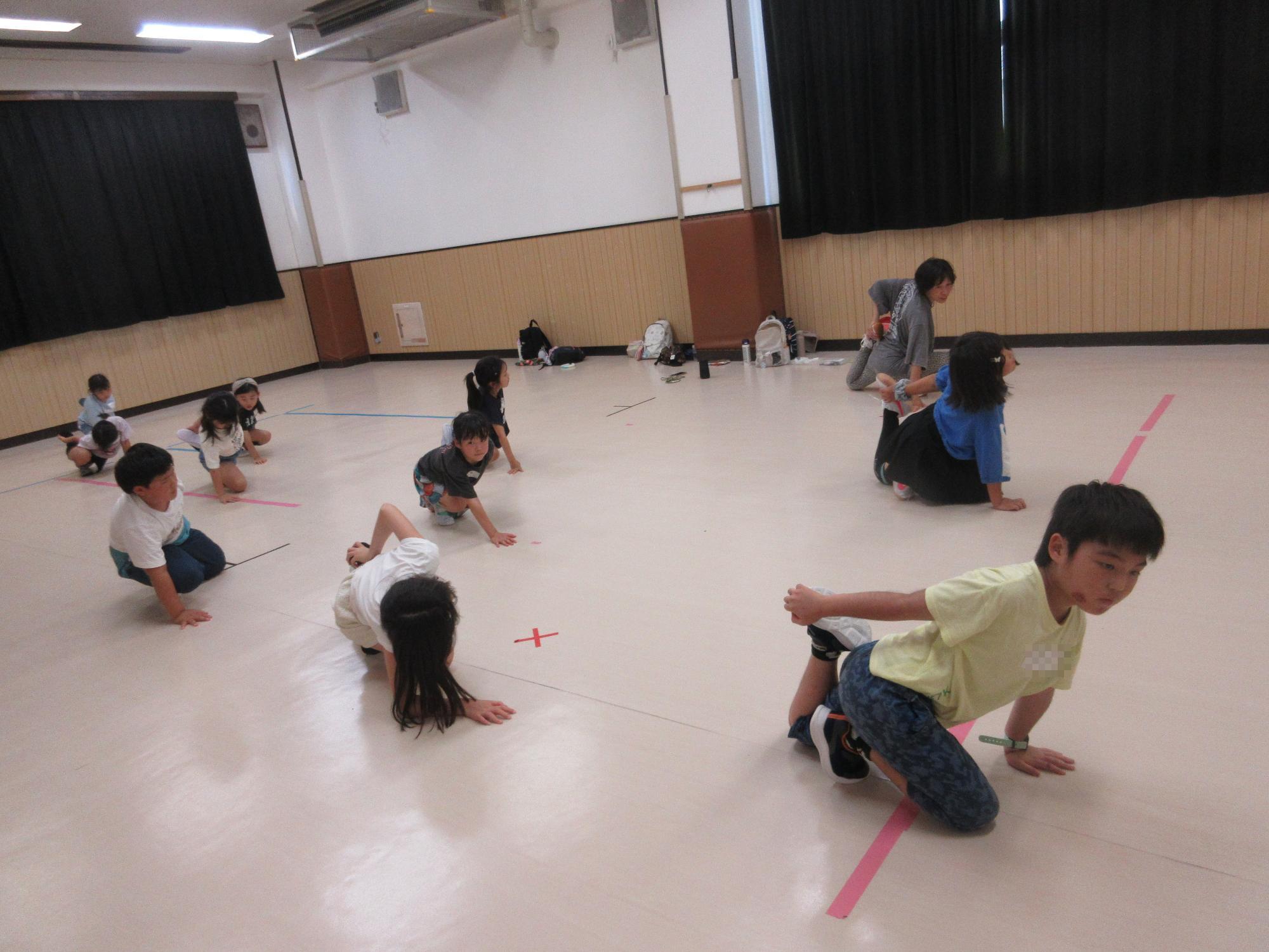 ホールで床に膝と手をつき右手で左足つま先を持ちストレッチをしているところ