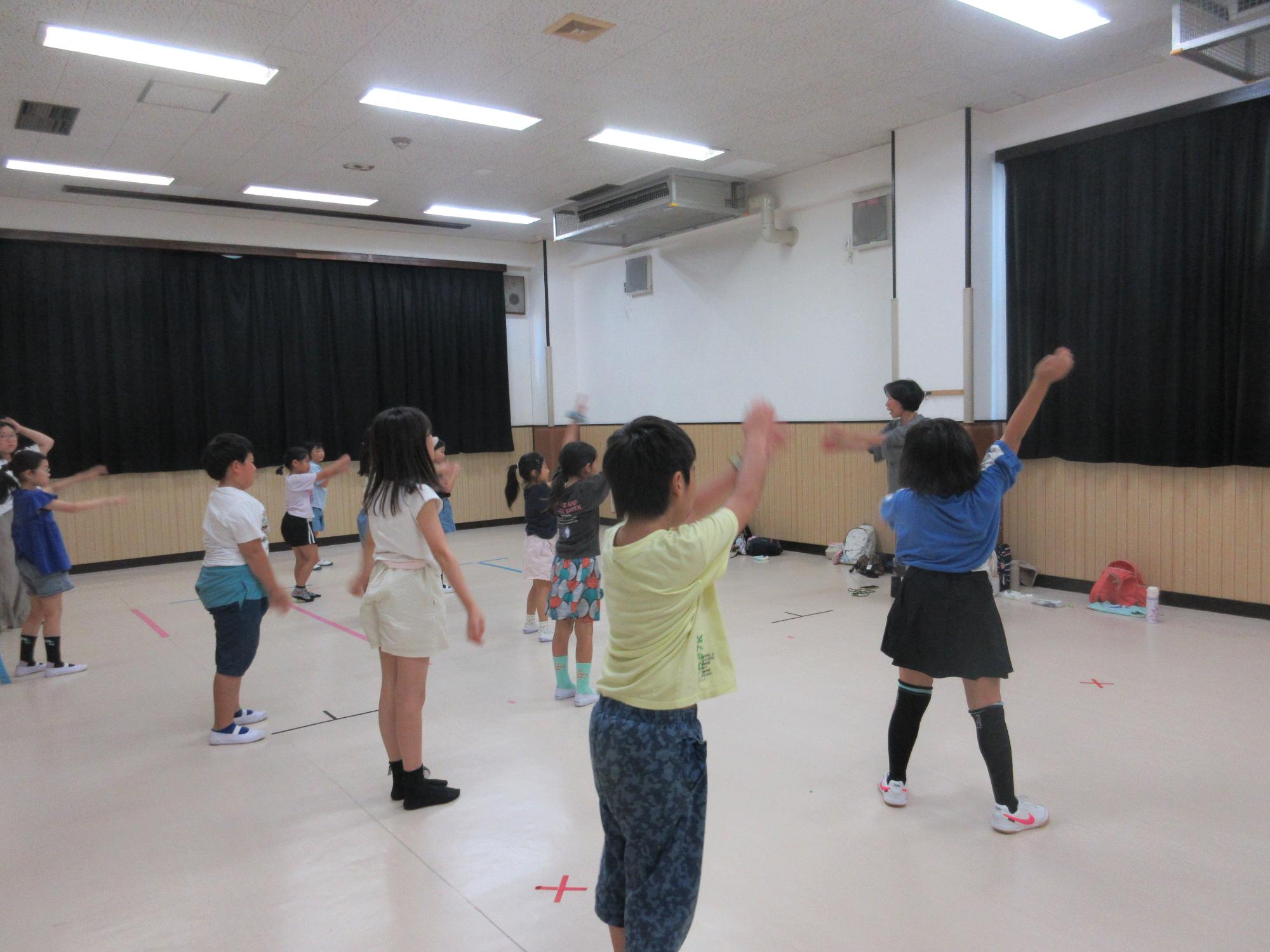 講師を前に二列に並び手を上げ下げしてダンスをする子どもたち