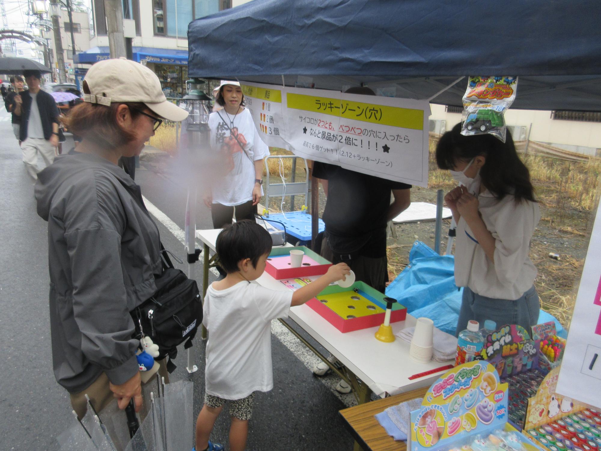 6個穴が開いた30cm四方の箱にカップに入ったサイコロを転がす幼児