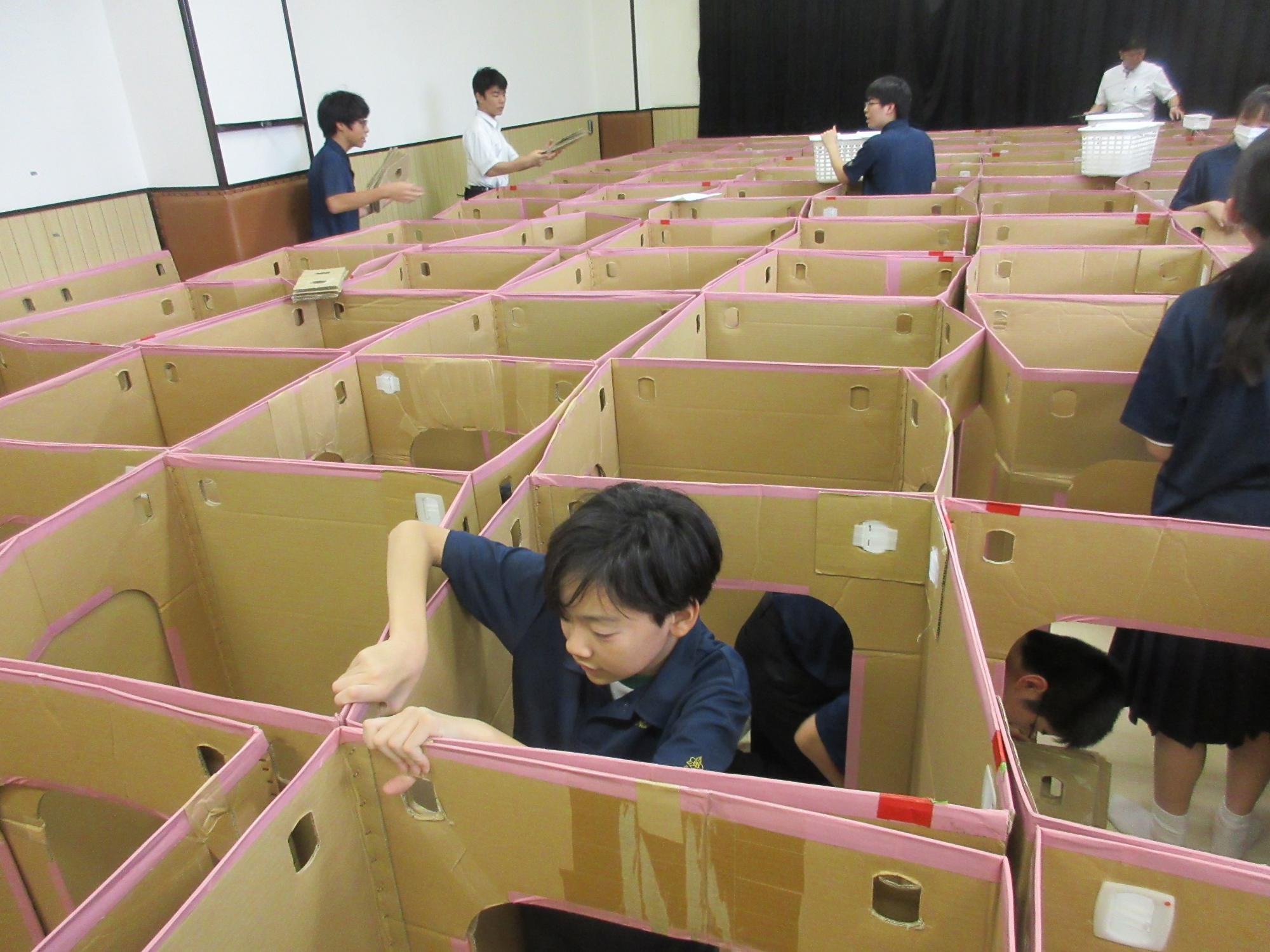 めいろの中に入りダンボールの四隅をジョイントパーツでつなげる中学生