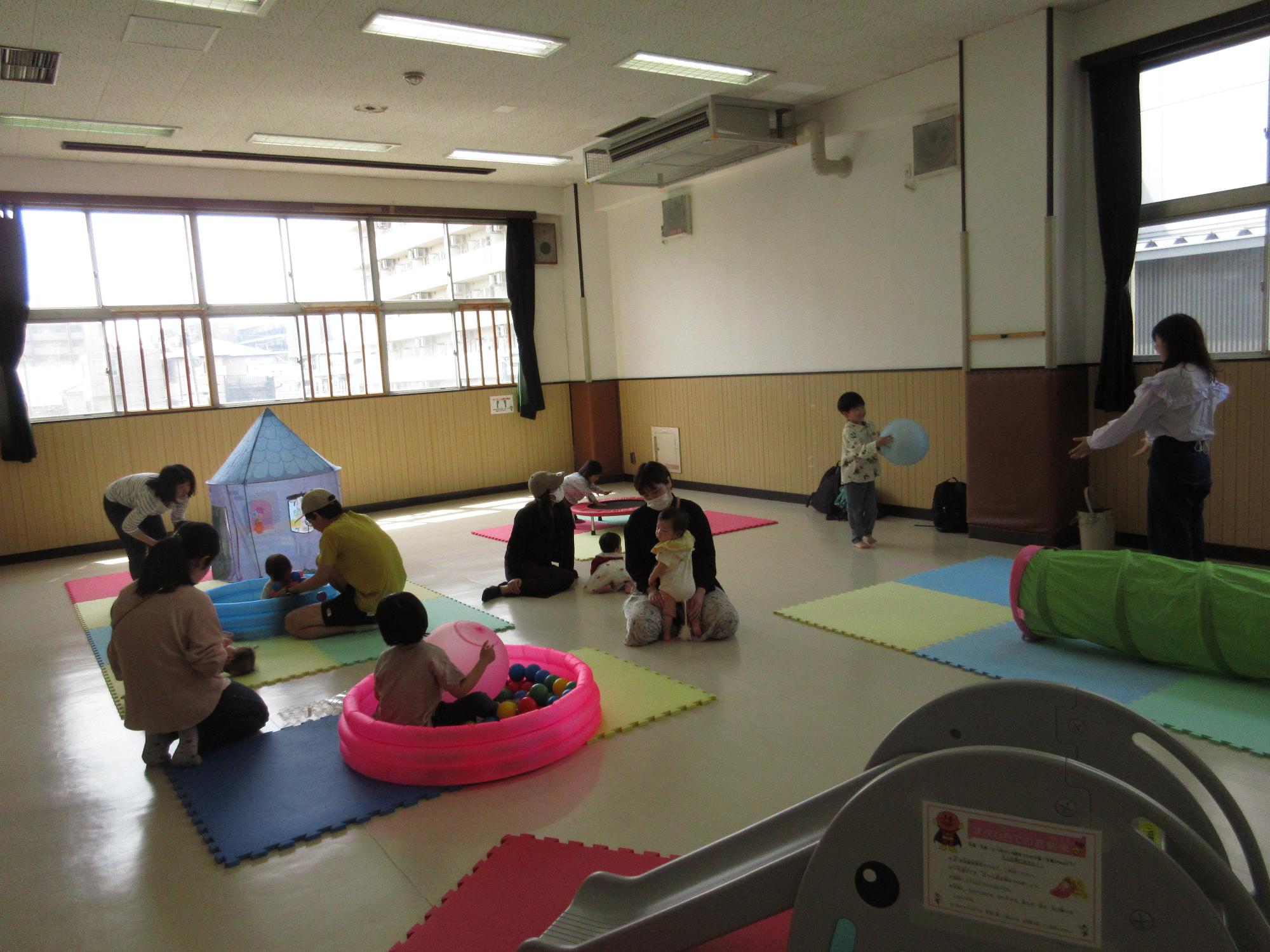 広いお部屋に置かれたおもちゃで子どもと大人が遊んでいる写真。