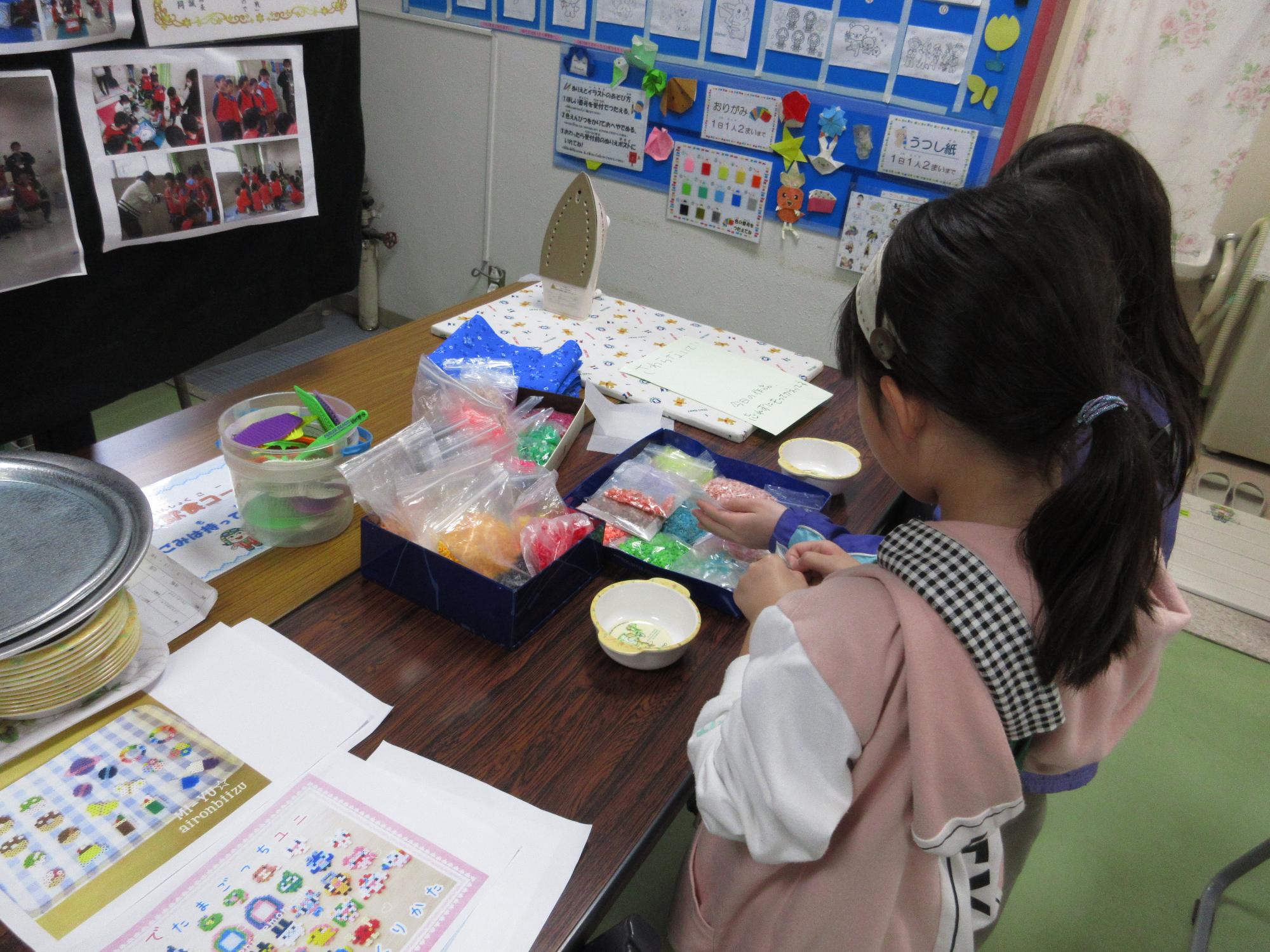 子どもが机にあるたくさんのビーズを選んでいる写真