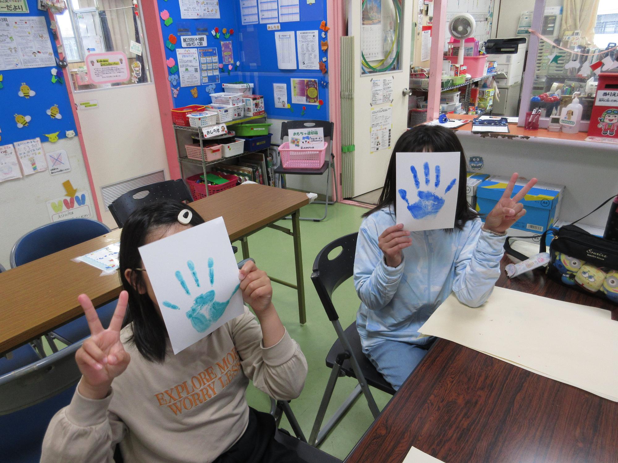 2人の子どもが自分の押した手形スタンプをピースしながら見せている写真