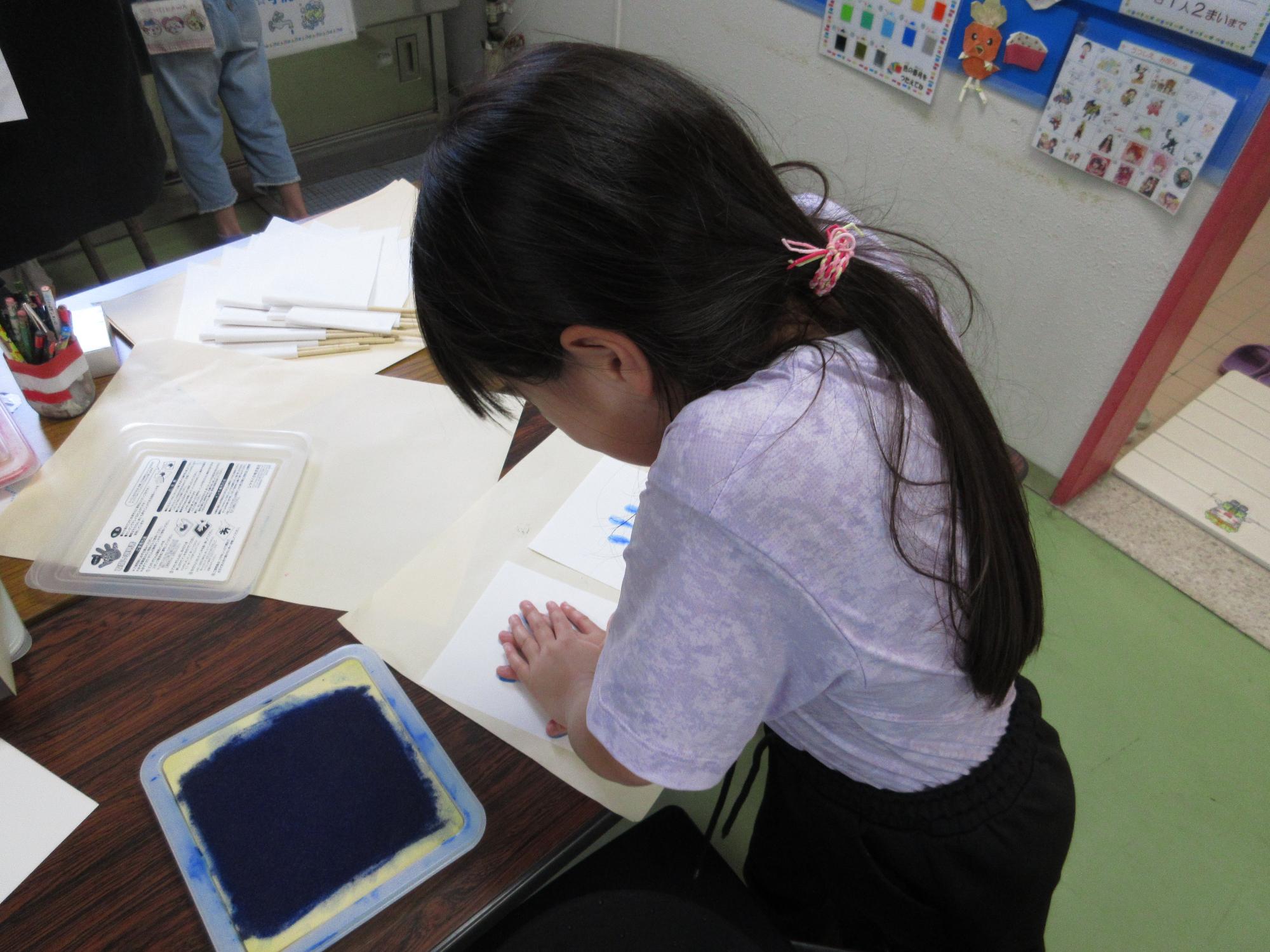 子どもがスタンプを付けた手を紙に押している写真