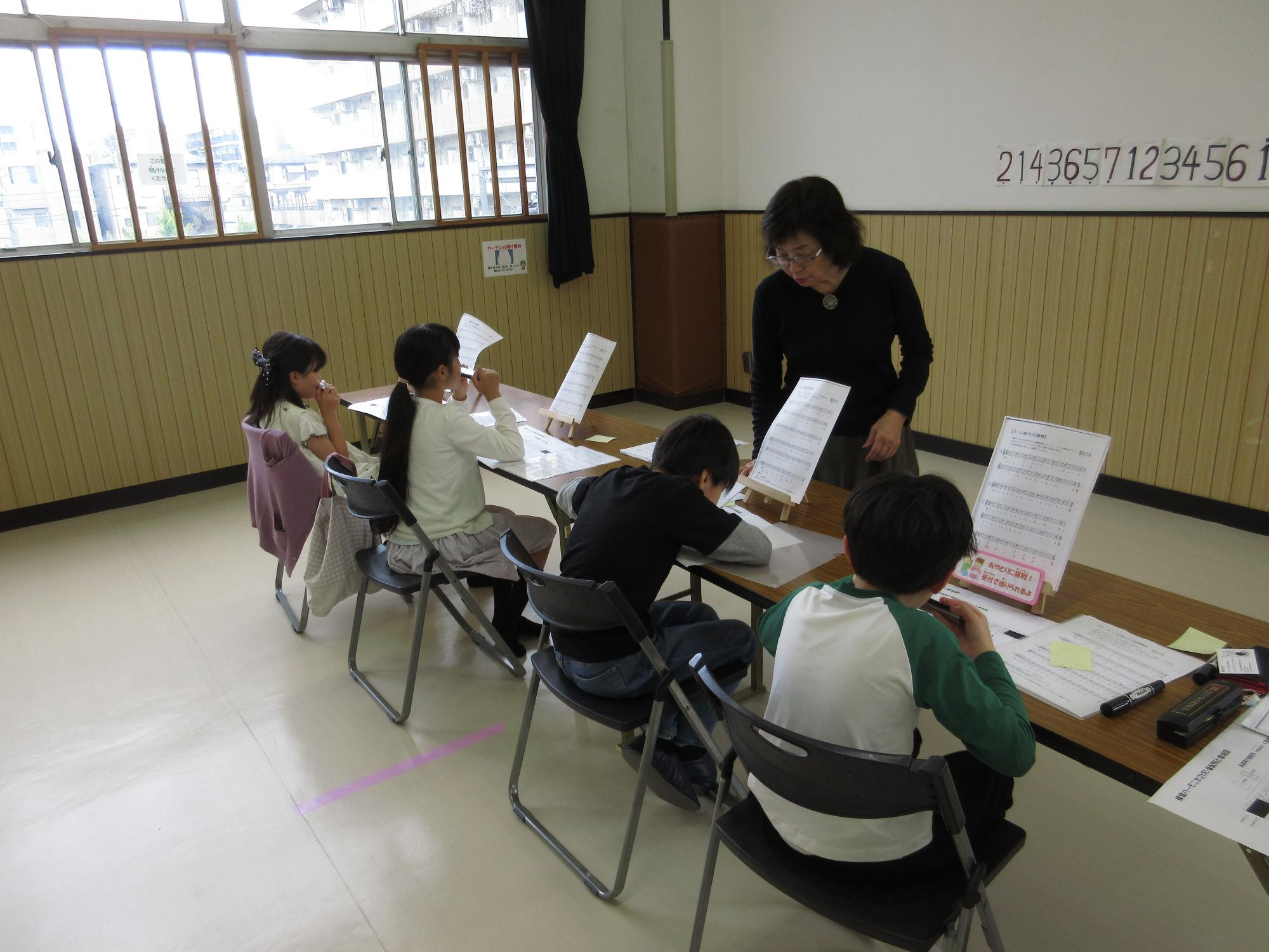 4人の子ども達が先生からハーモニカを教わっている写真