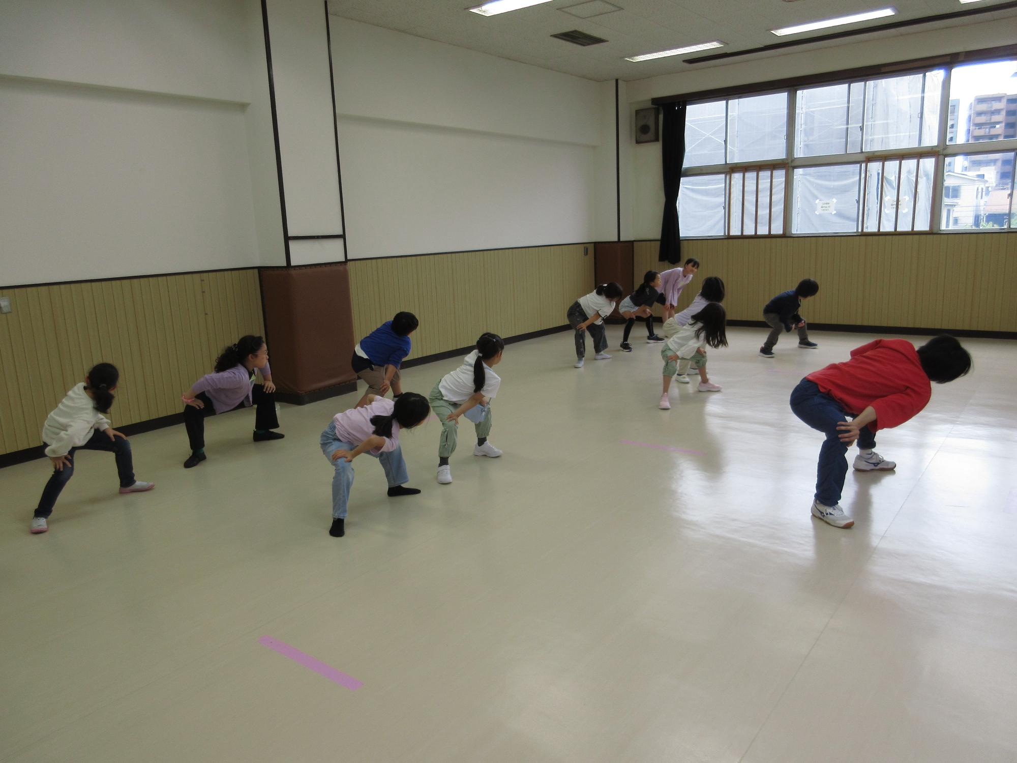 広いお部屋で講師の人に続いて子どもたちが柔軟をしている写真