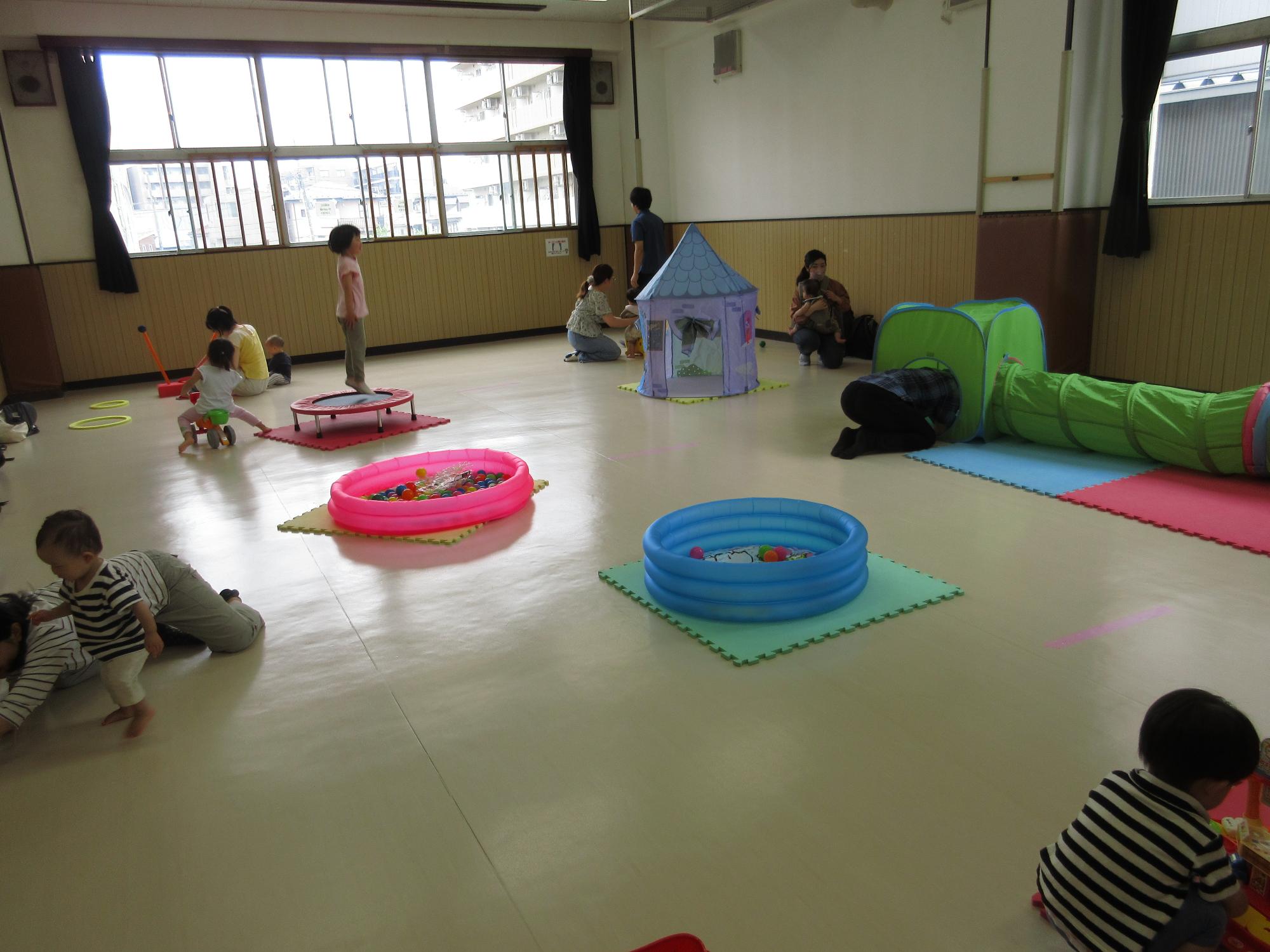 広いお部屋に置かれたおもちゃで乳幼児さん達が遊んでいる写真