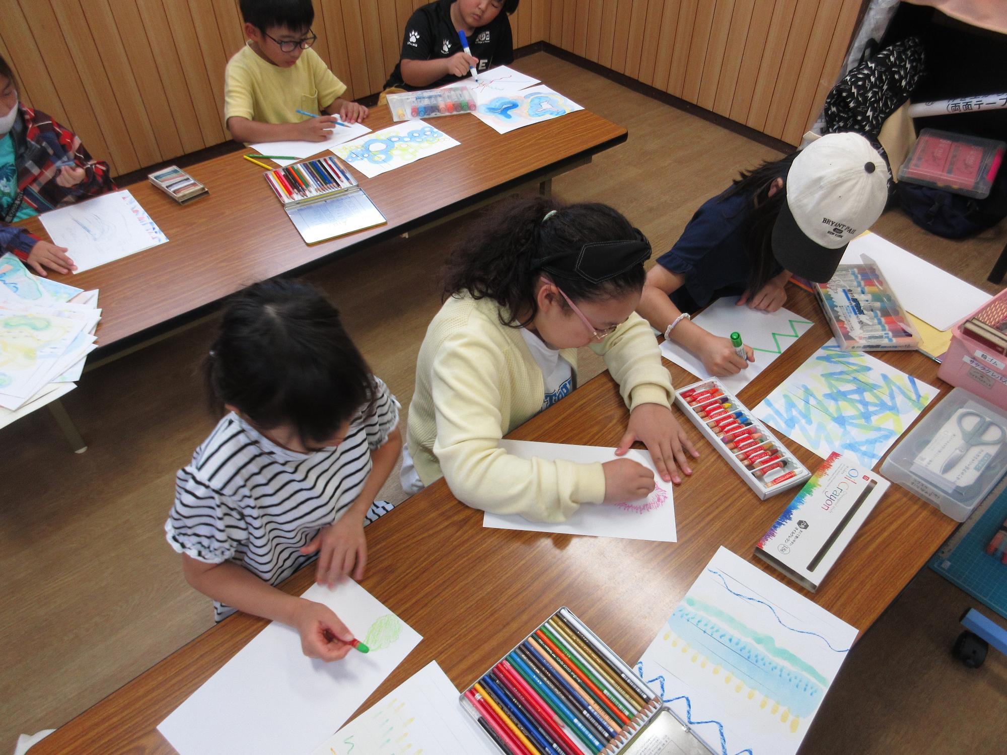 子どもたちが画用紙にペンやクレヨン、色鉛筆などで絵を描いている写真