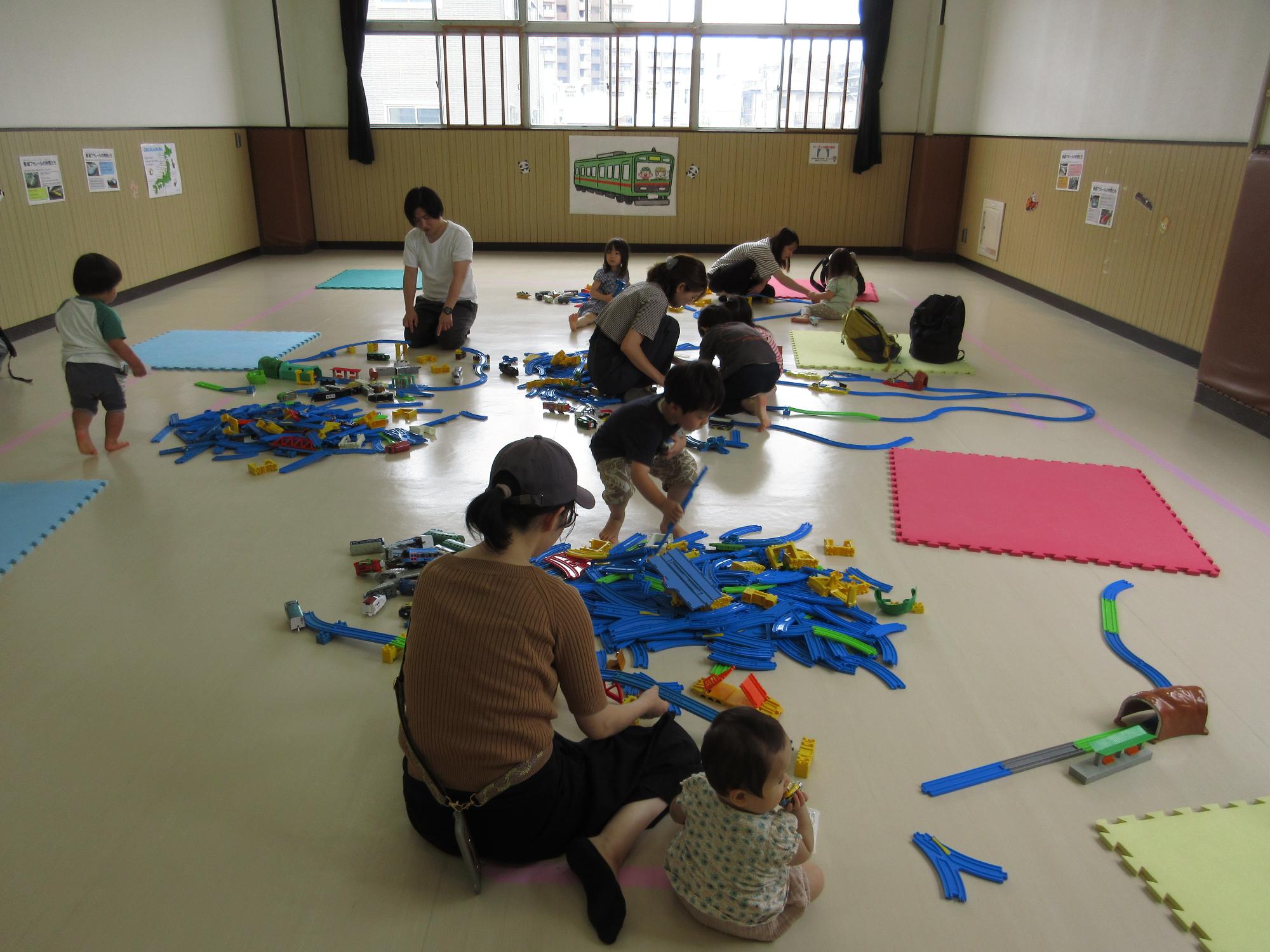集会室にたくさんのレールを幼児親子がつなげている写真