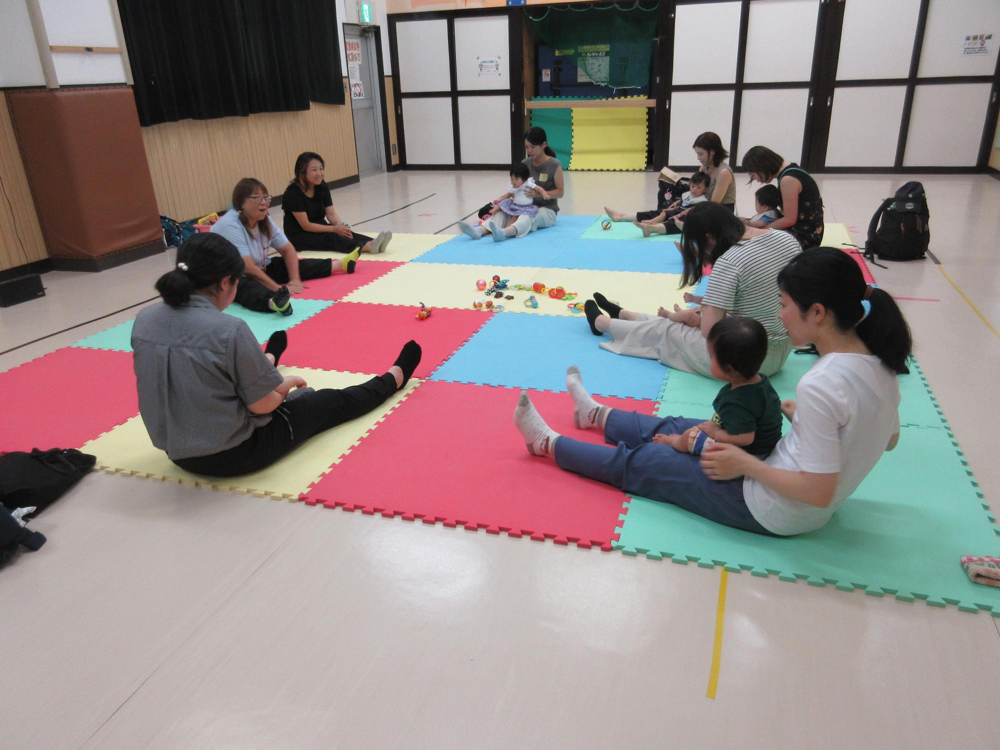 いしちゃんとさち先生と一緒にマットの上で親子体操をしているところ