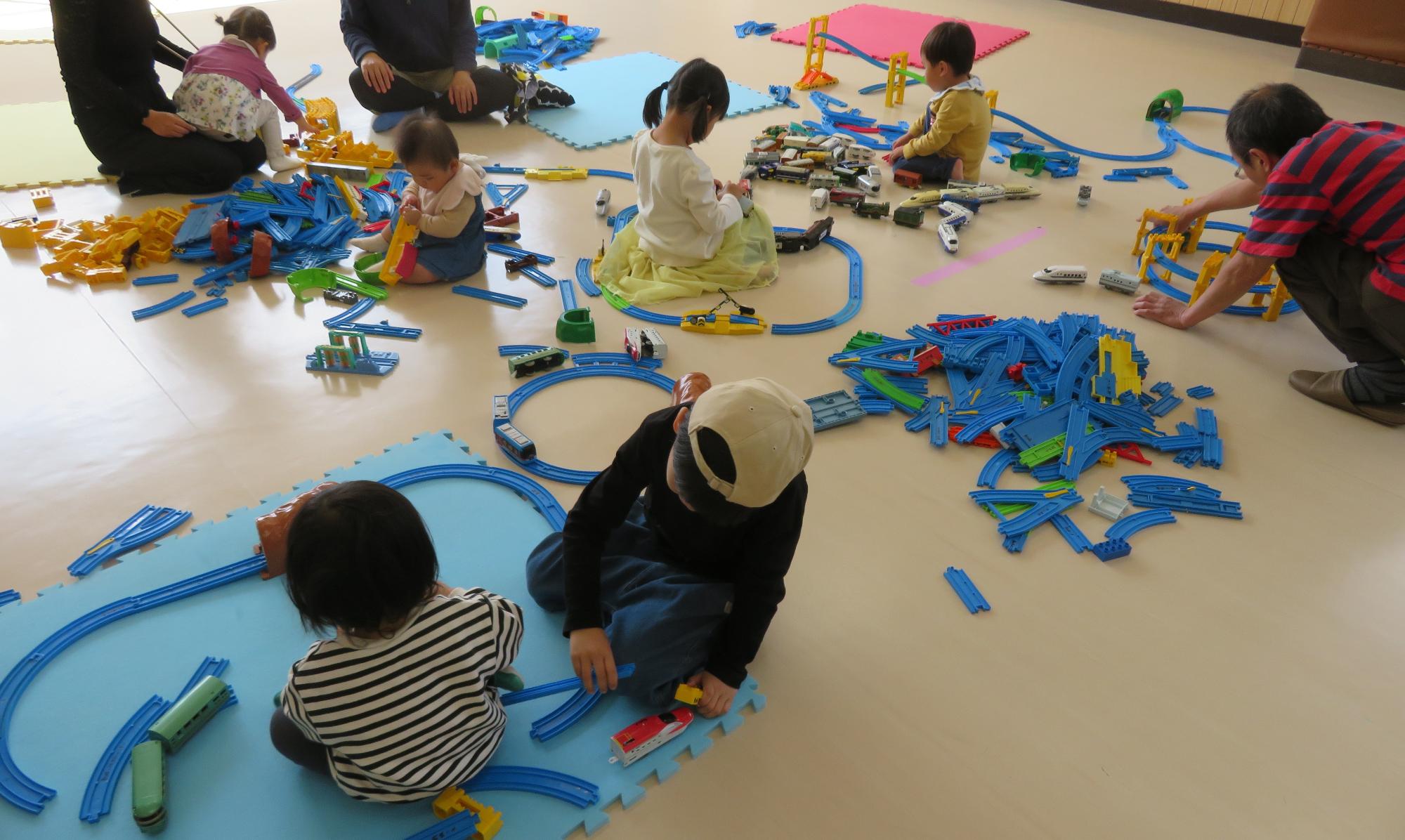 子どもたちが、広い部屋に用意されたレールをつなげている写真