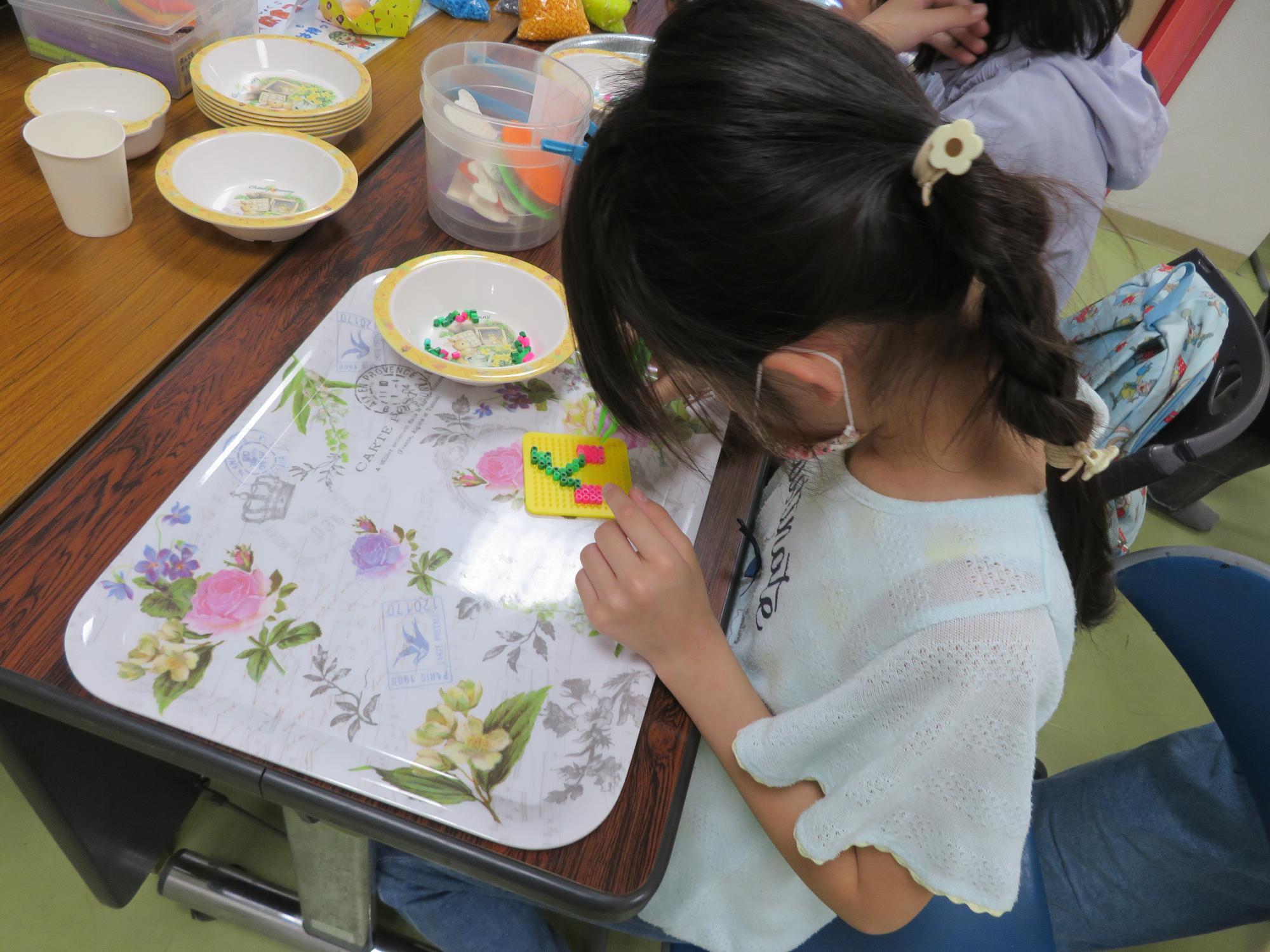 子どもがピンセットでアイロンビーズを並べている写真
