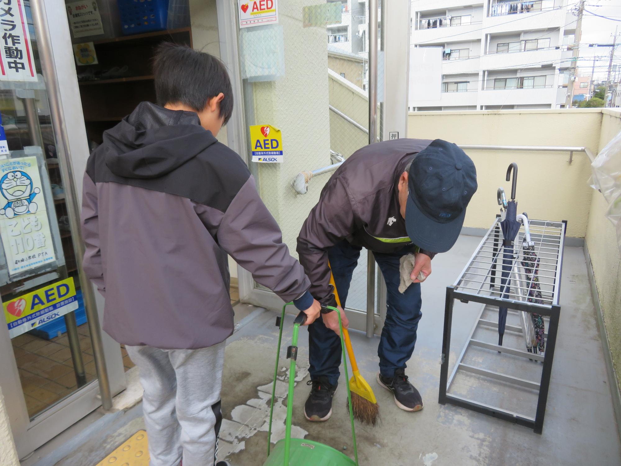 おとなとこどもがホウキとちり取りで玄関を掃除しています