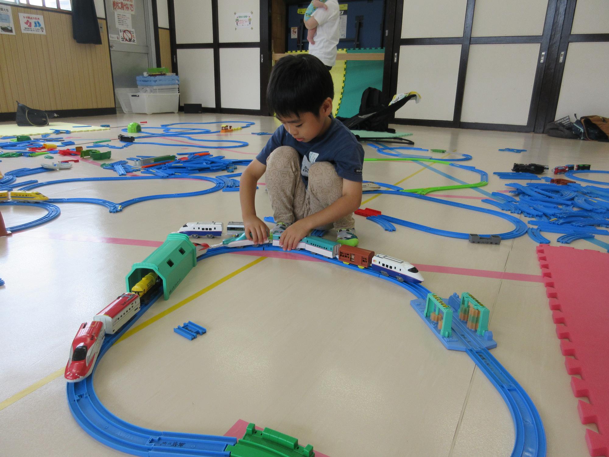 自分で作った線路に沢山の電車を走らせるこども