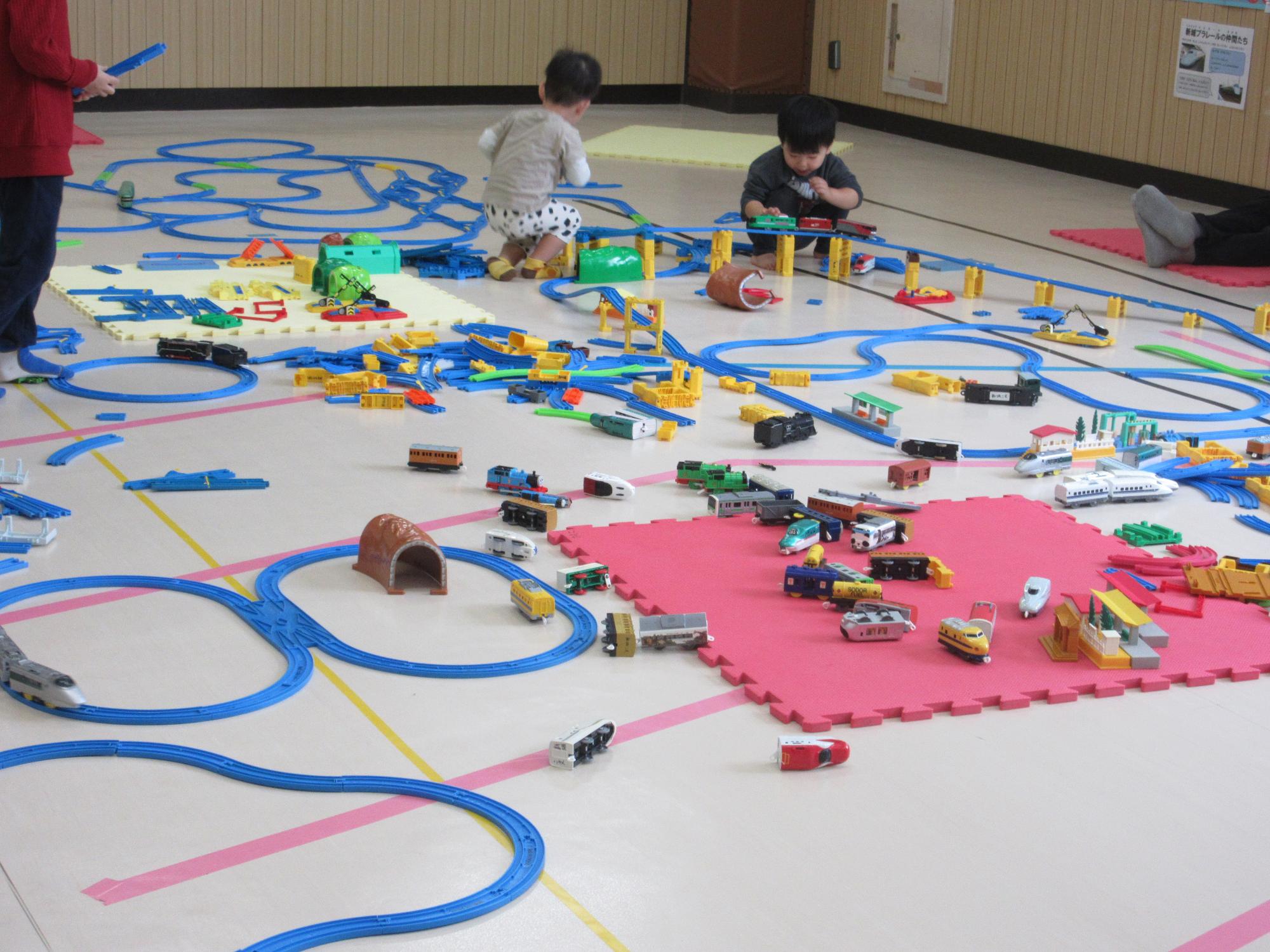 集会室いっぱいに線路を広げて楽しむ乳幼児親子