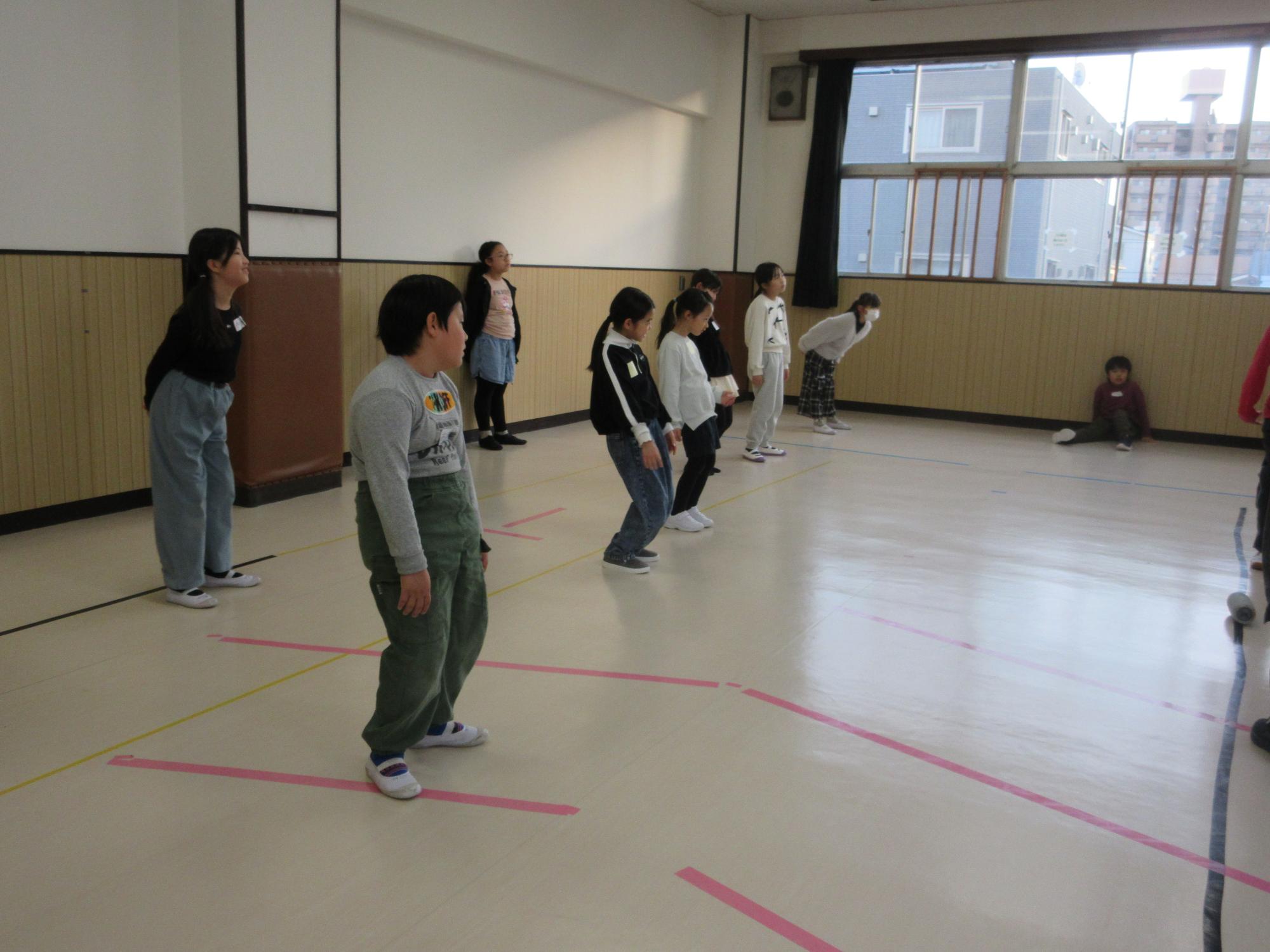 立ってひざを曲げ伸ばししてダンスの練習をする子どもたち