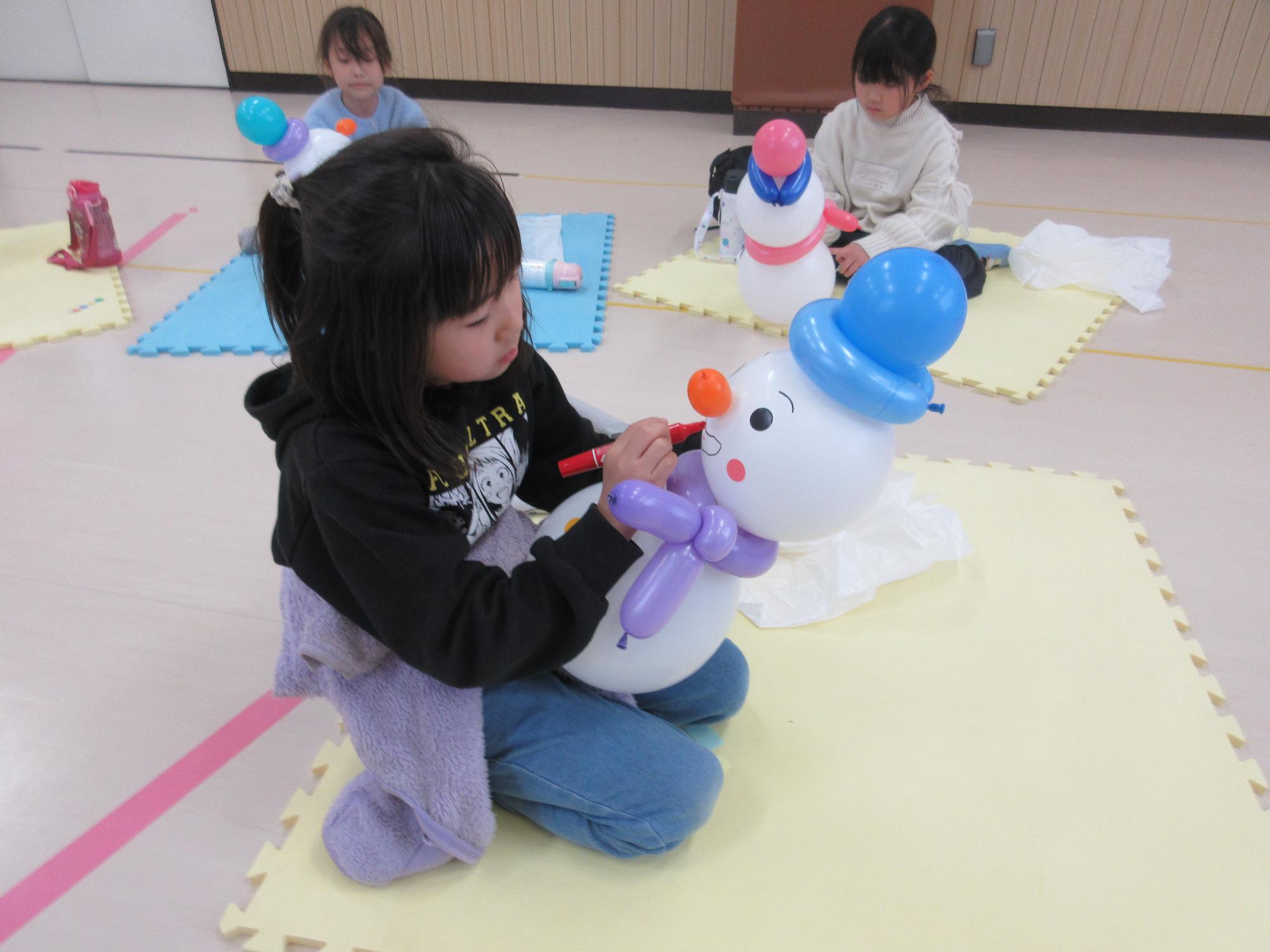 風船に丸いシールを貼りペンで顔を描いているところ