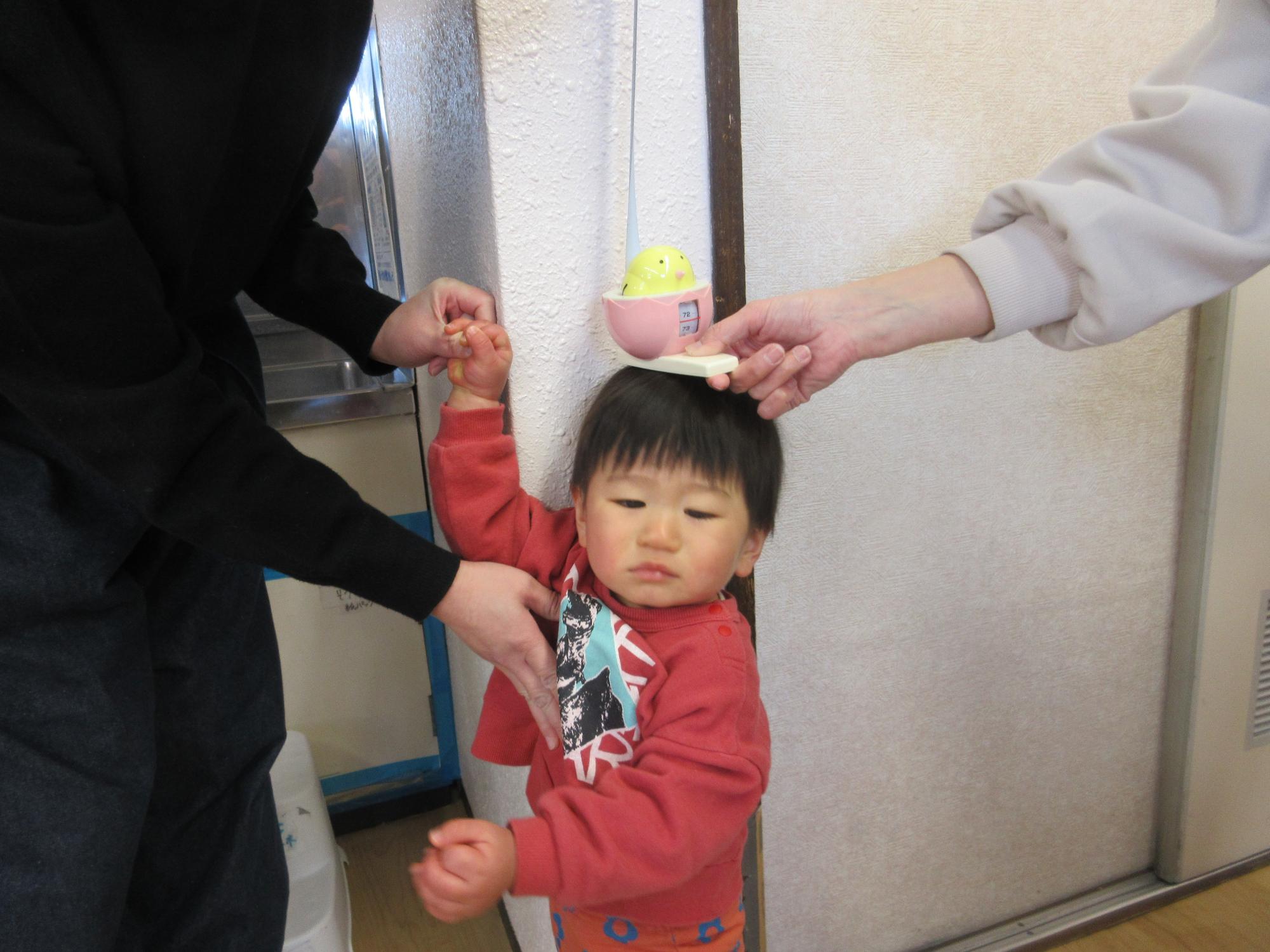 頭の上にひよこの測定器を当てて、立って身長を測る子ども