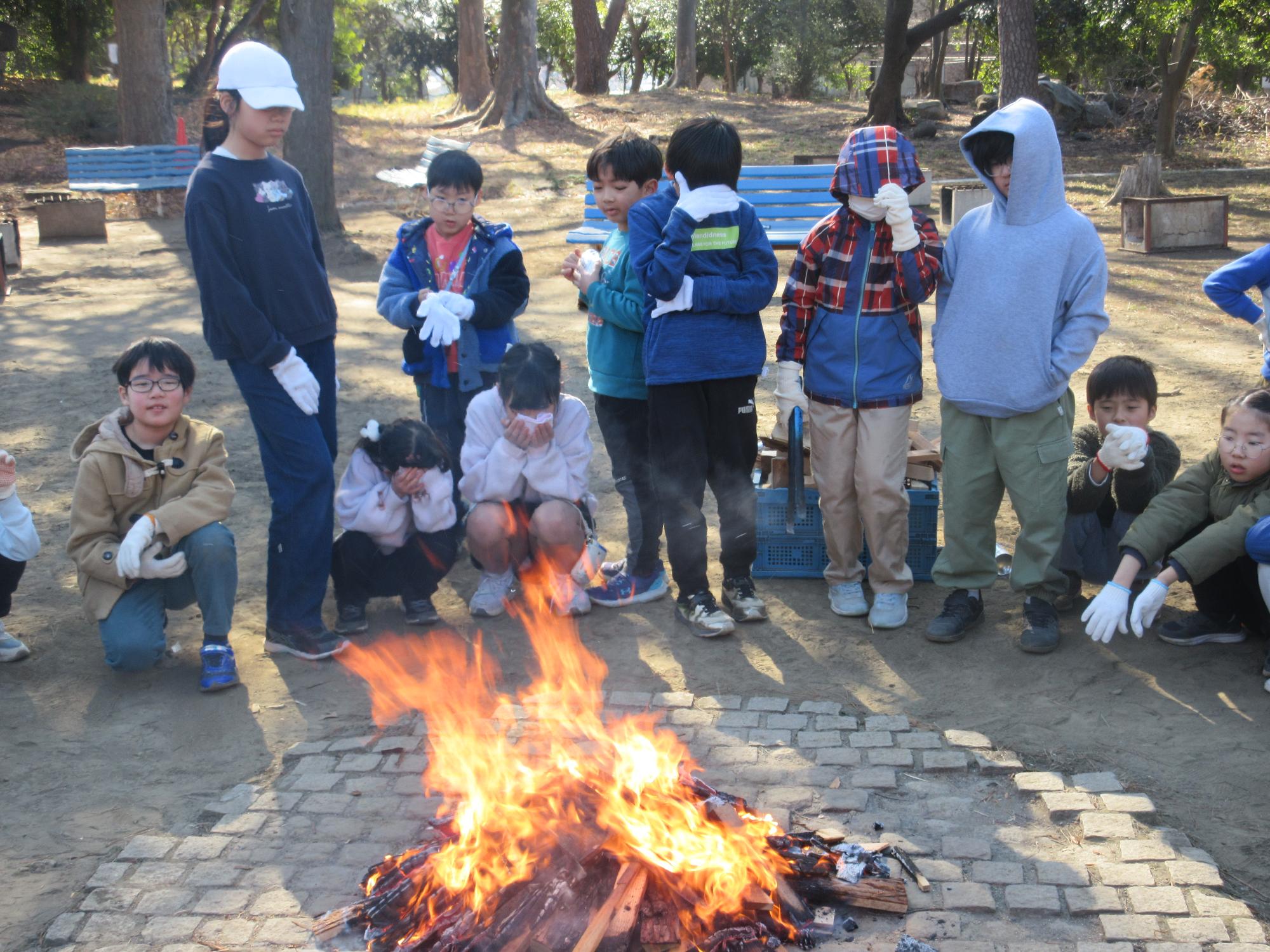 焚き火の熱さに顔を覆う子どもたち