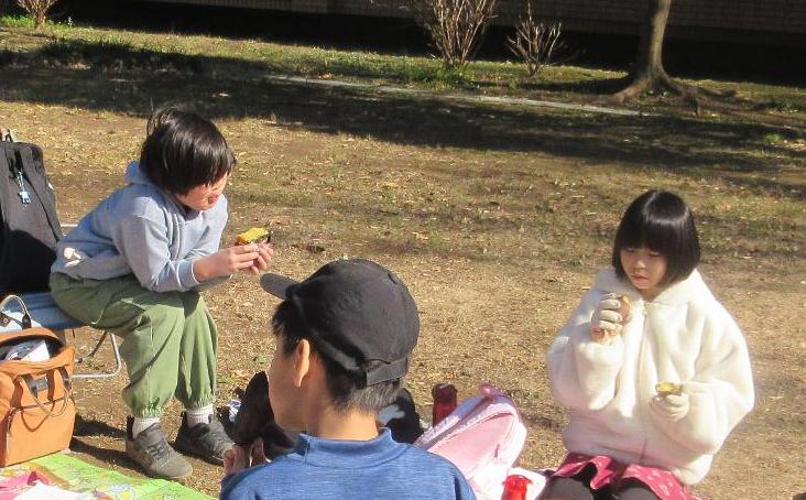公園の芝生でやきいもを食べる子どもたち