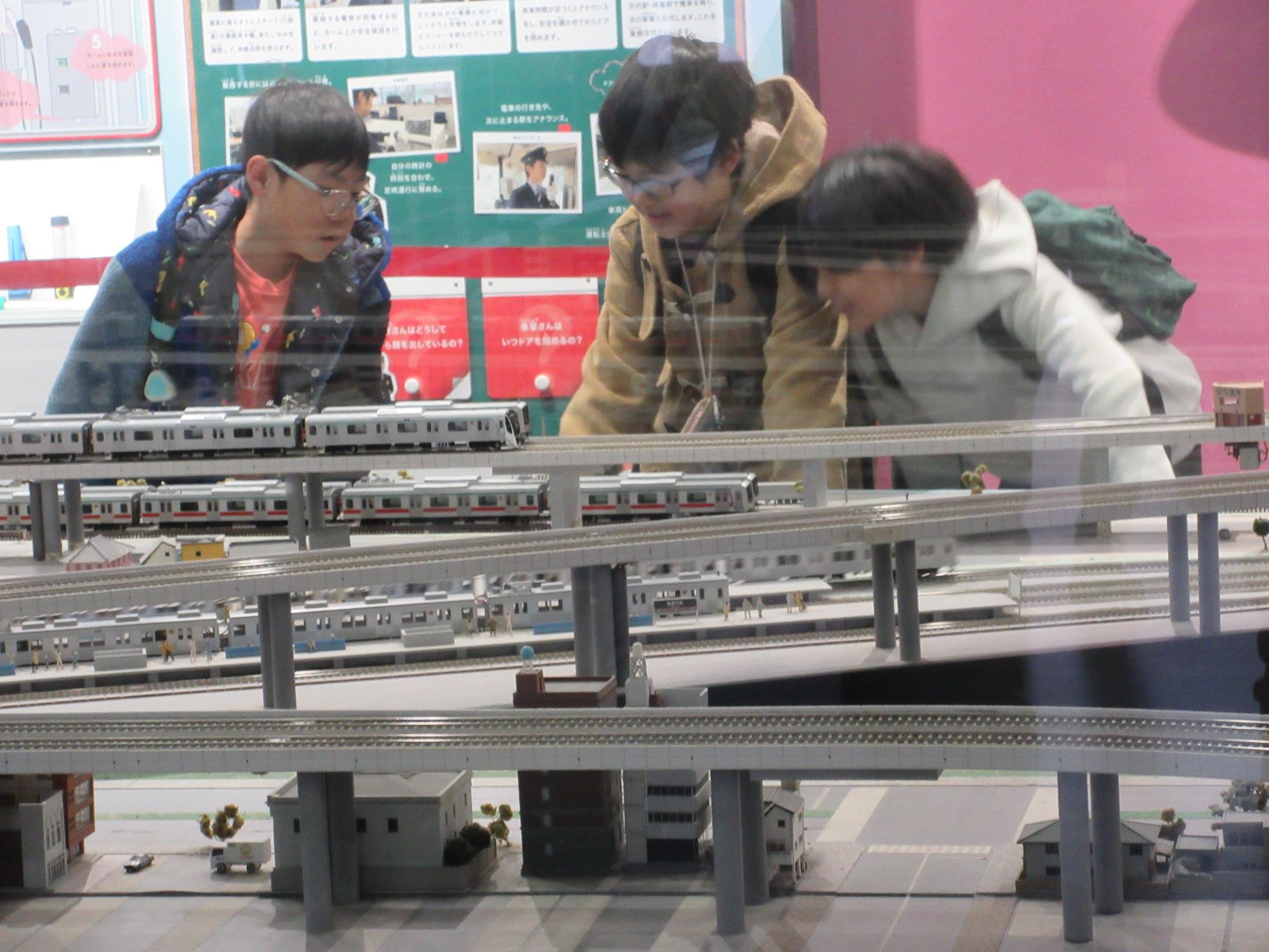 博物館で模型のレールを走る電車を眺める子どもたち