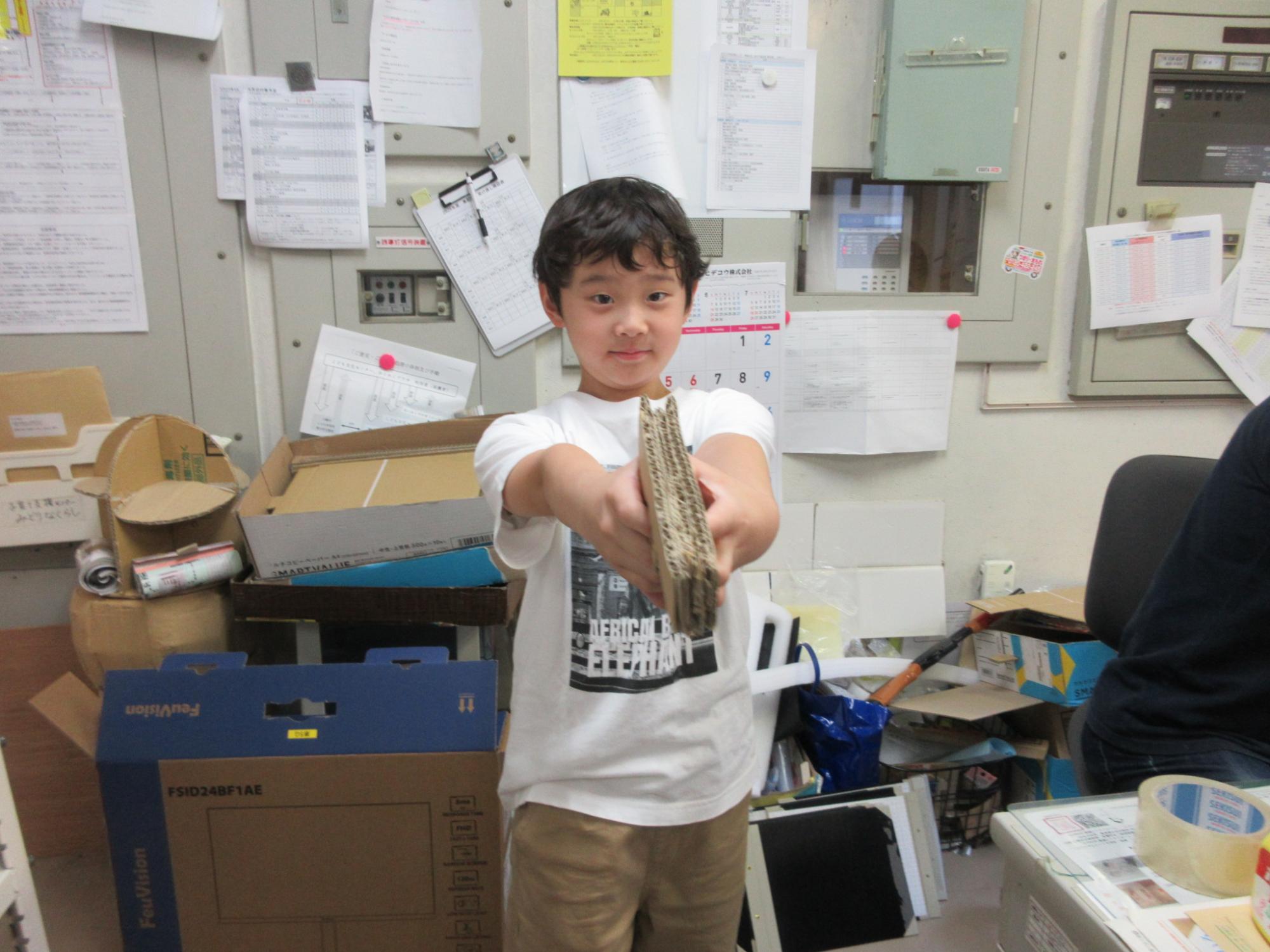 自分で完成させたダンボール銃を構える小学生の様子の写真